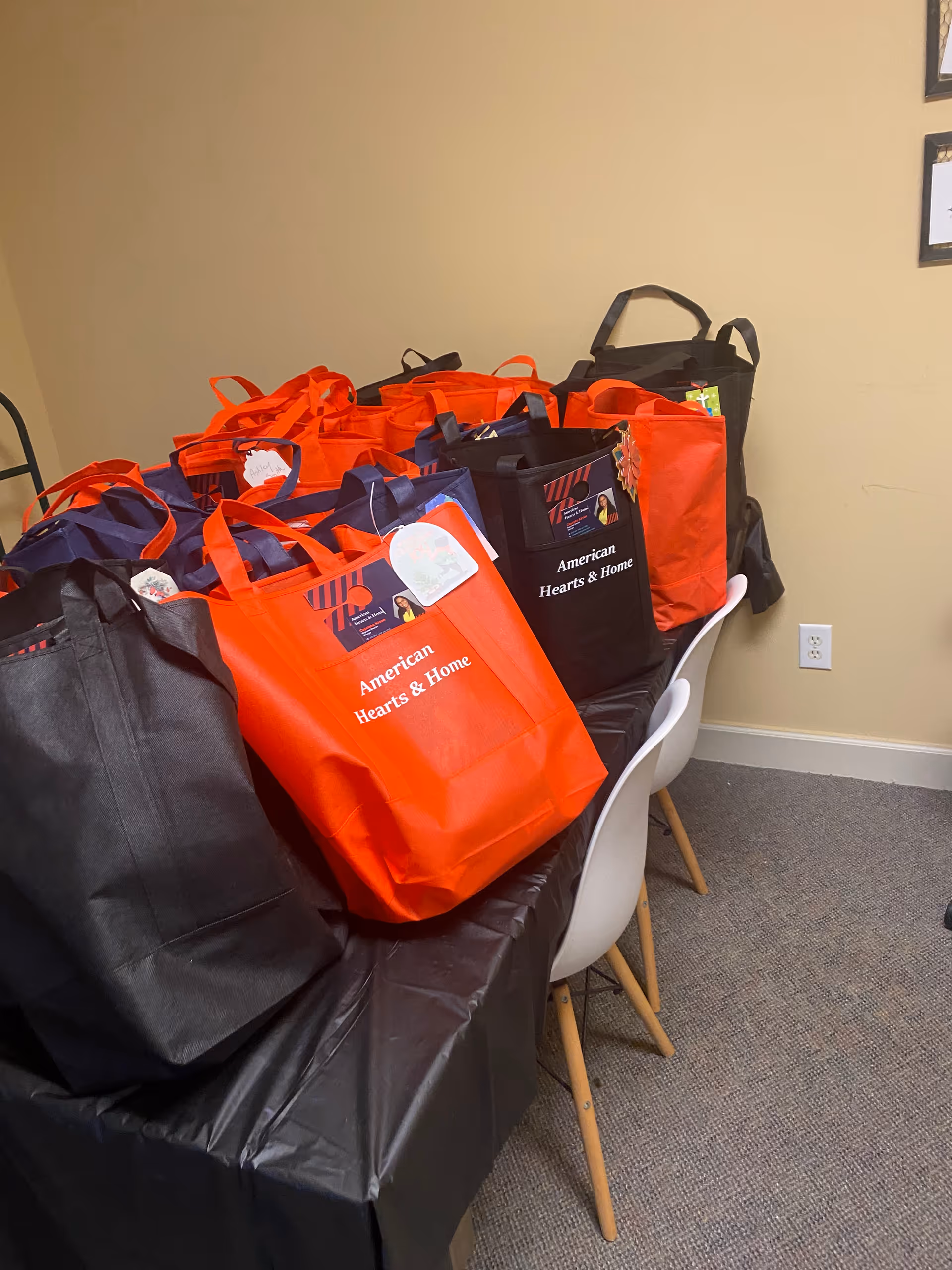 Bright orange and black American Hearts and Home bags lined up on a table indoors.