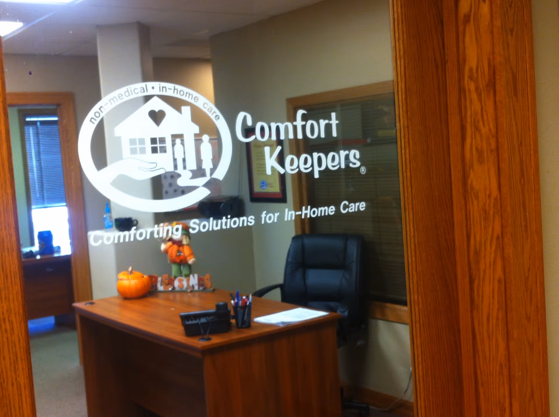 Inside a reception area with a desk, chair, pumpkins, and Comfort Keepers signage on glass.