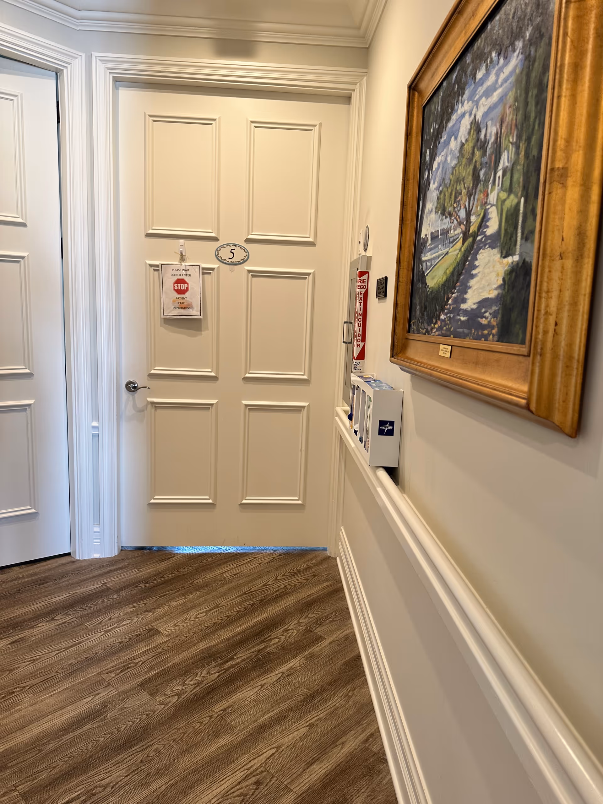 A hallway inside a senior living facility with paneled doors and a framed painting.
