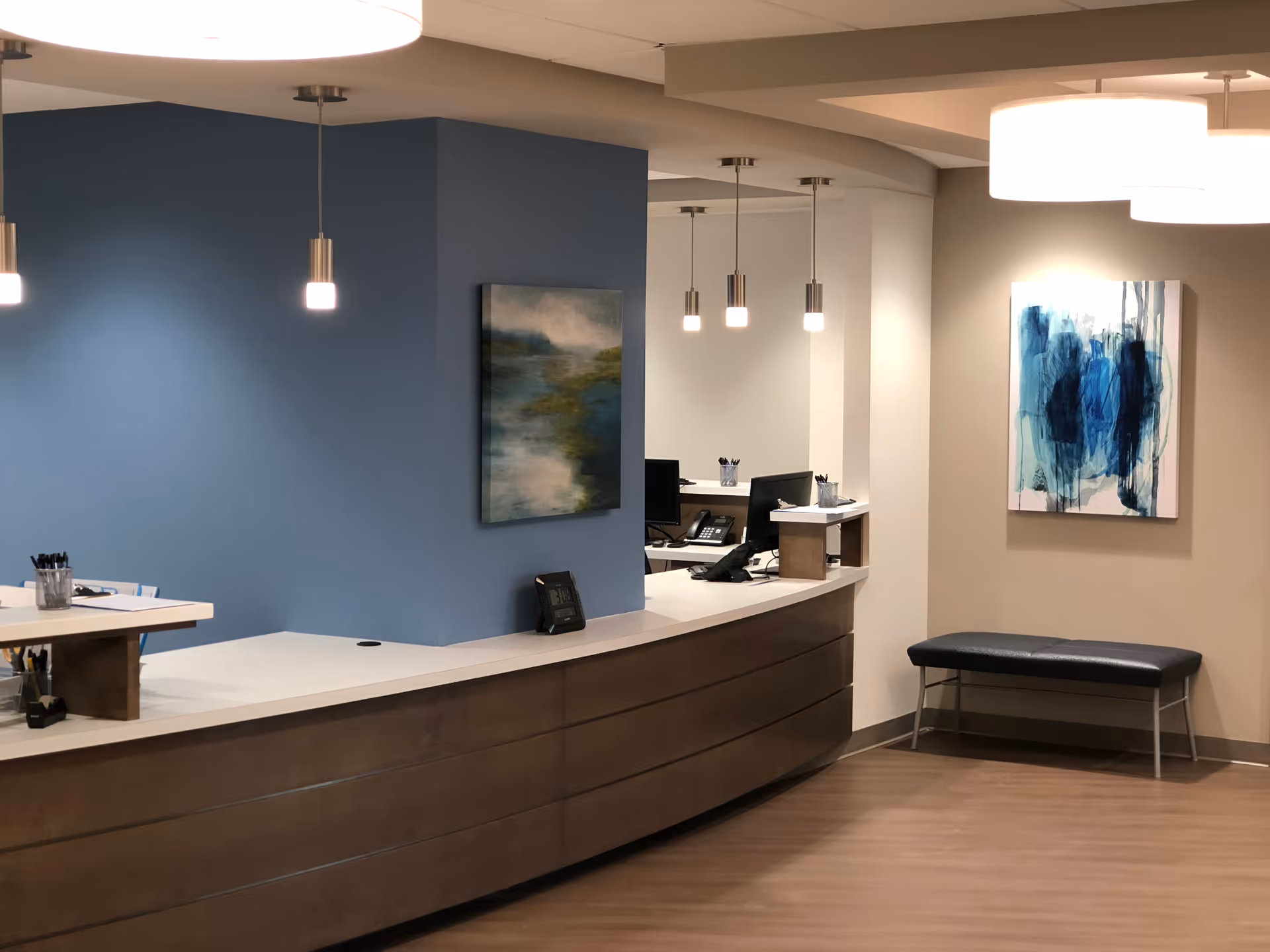 Reception desk along a blue accent wall with pendant lights, art, and a bench.