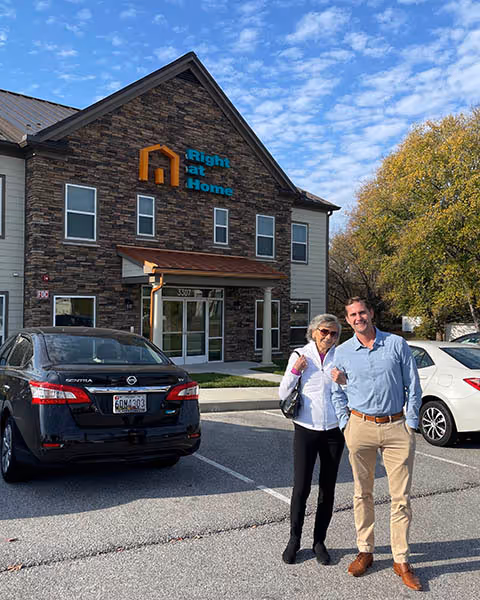 Two people stand in a parking lot in front of Right at Home senior living facility.
