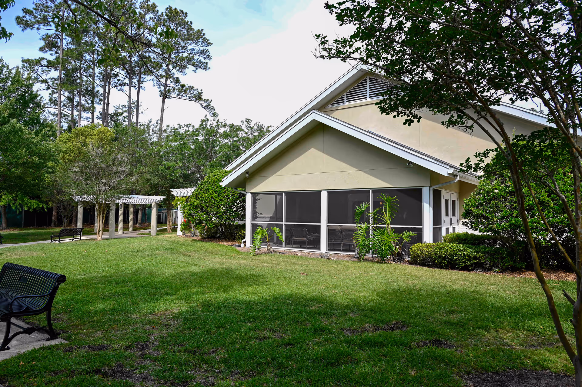 A single-story beige building with a screened porch and green lawn in a park-like yard.