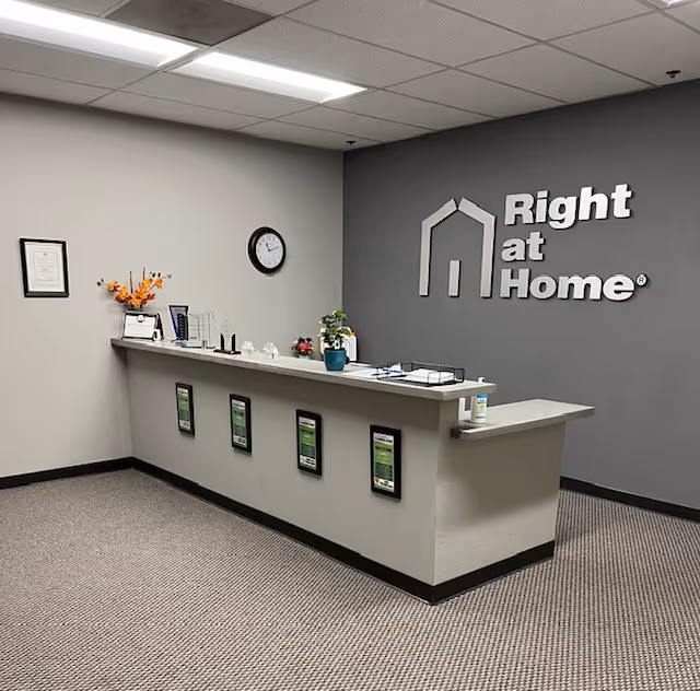 Reception desk in a Right at Home facility lobby with clock and logo on wall.