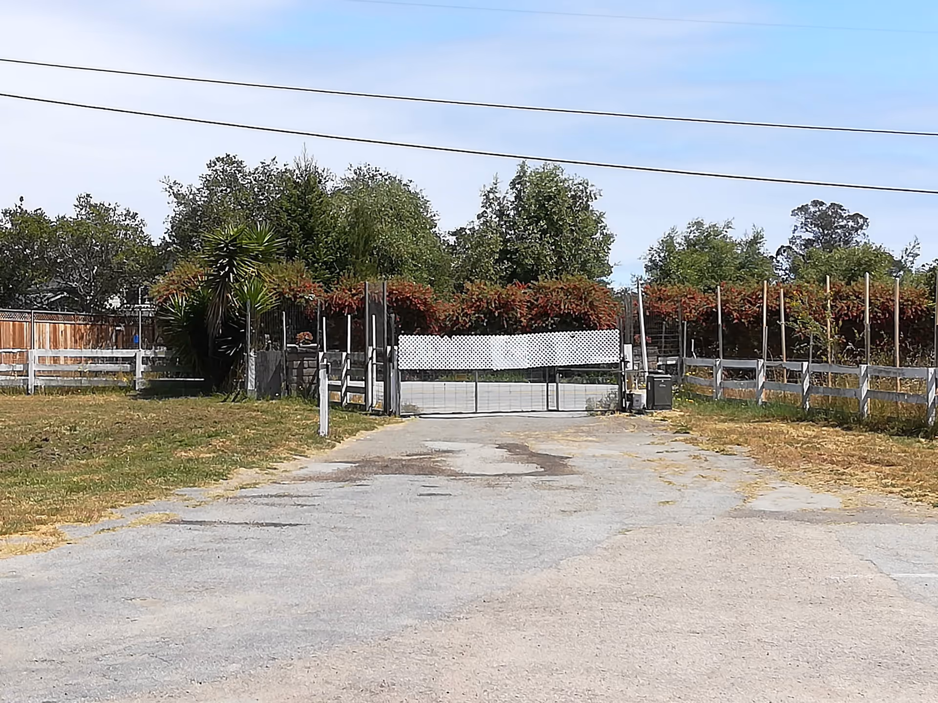 Gated entrance to Soquel Leisure Villa with a gravel driveway, fencing, and trees.