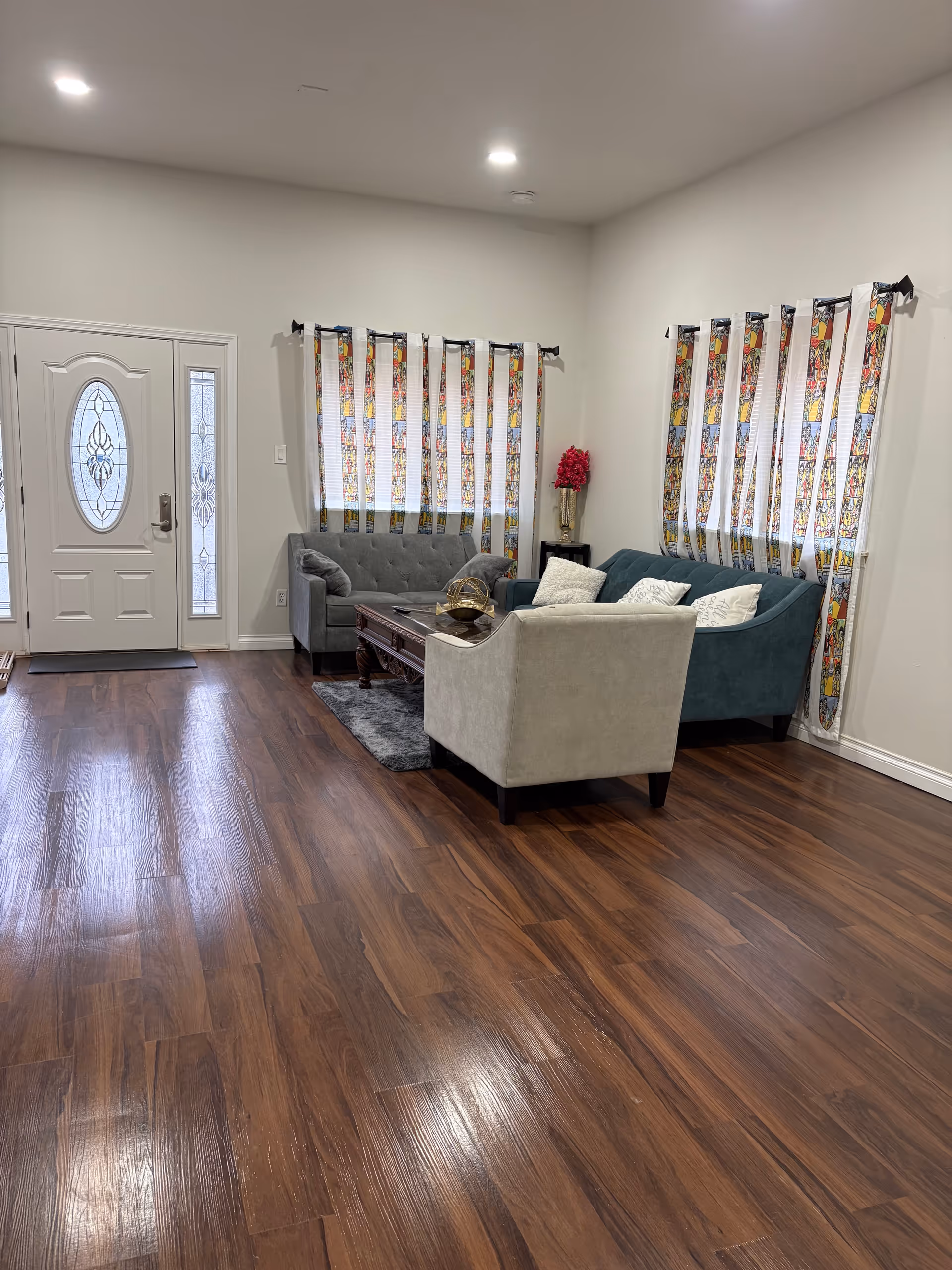 Cozy living room with blue and gray couches, coffee table, and colorful curtains.