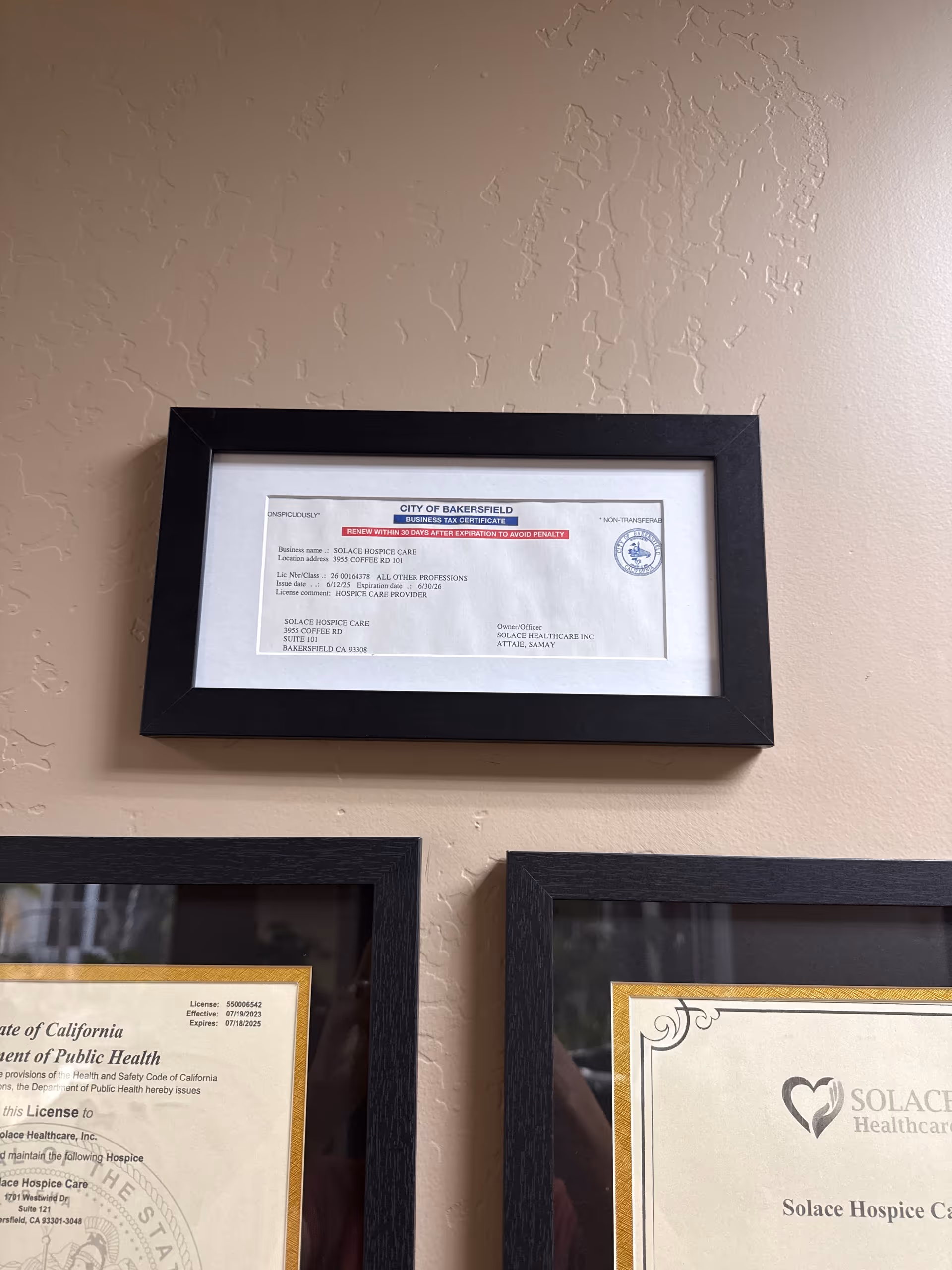 Framed certificates hang on a beige textured wall inside a facility.