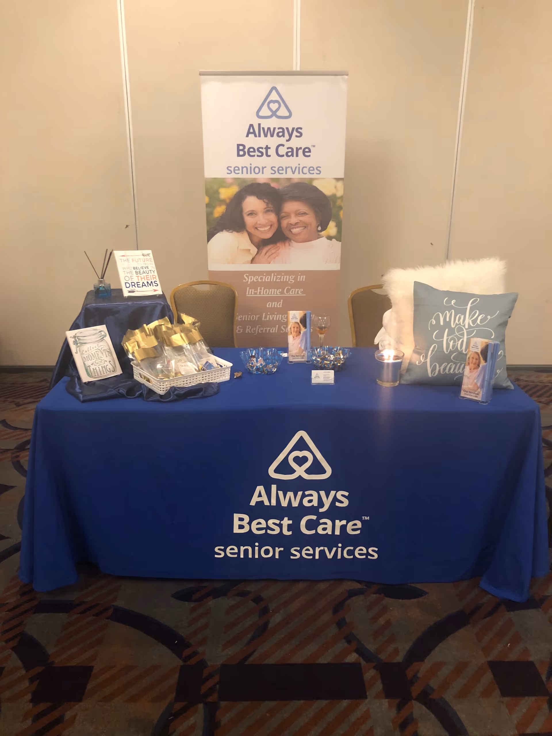 Booth setup featuring Always Best Care banner, blue tablecloth, and promotional materials.