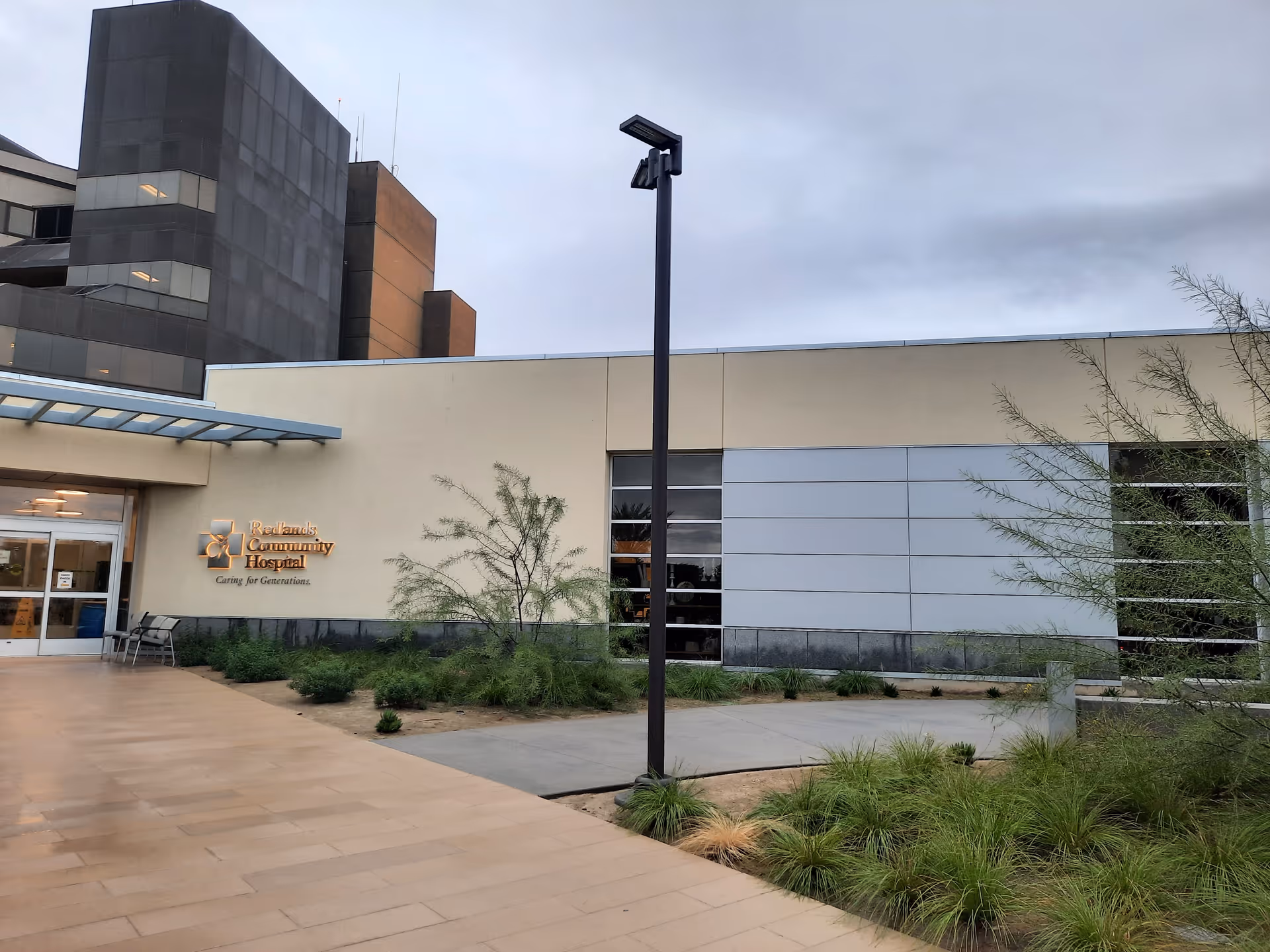 Exterior view of Redlands Community Hospital building with entrance, landscaping, and cloudy sky.