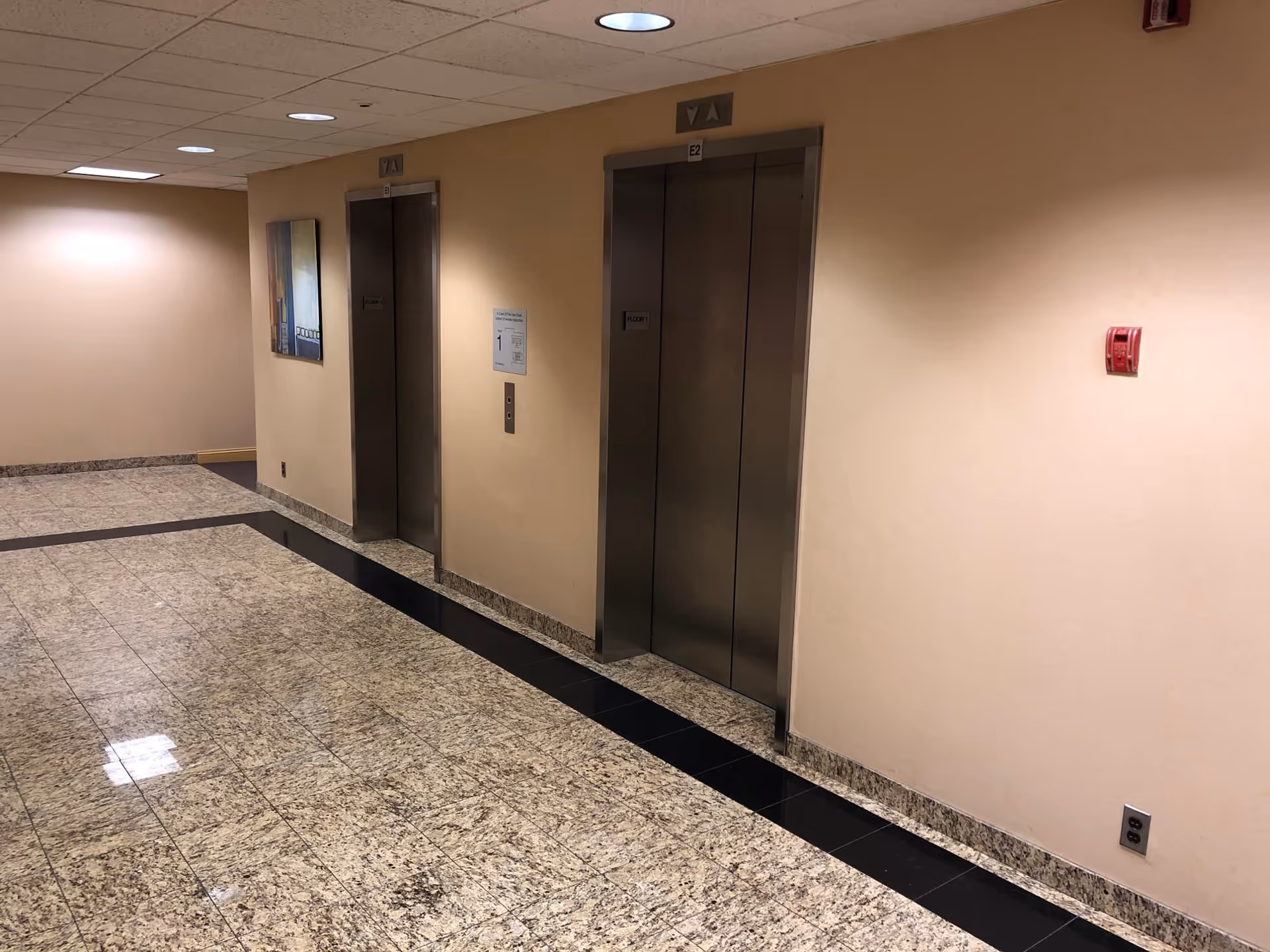 Interior hallway with two elevator doors, beige walls, and polished tile flooring.