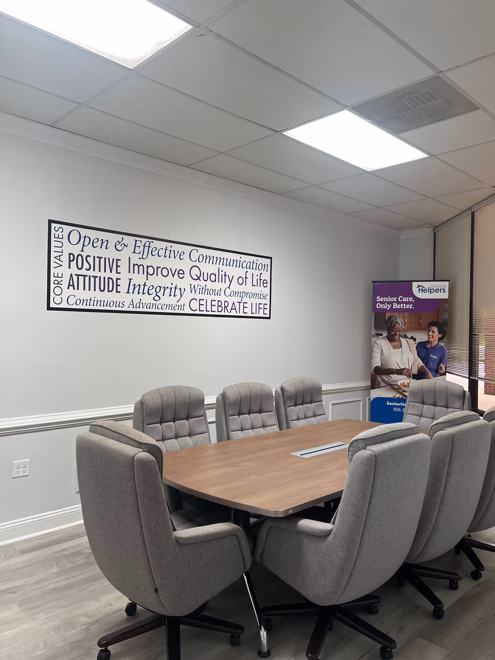 A conference room with a wooden table, gray swivel chairs, a wall sign, and banner.