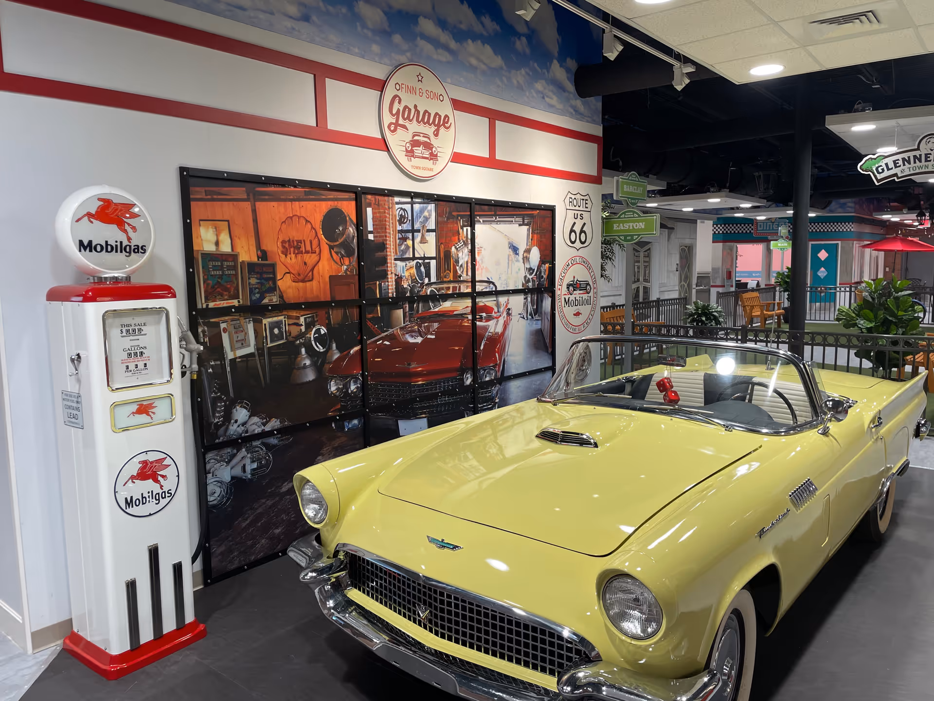 Retro yellow convertible car displayed indoors beside vintage gas pump and mural.