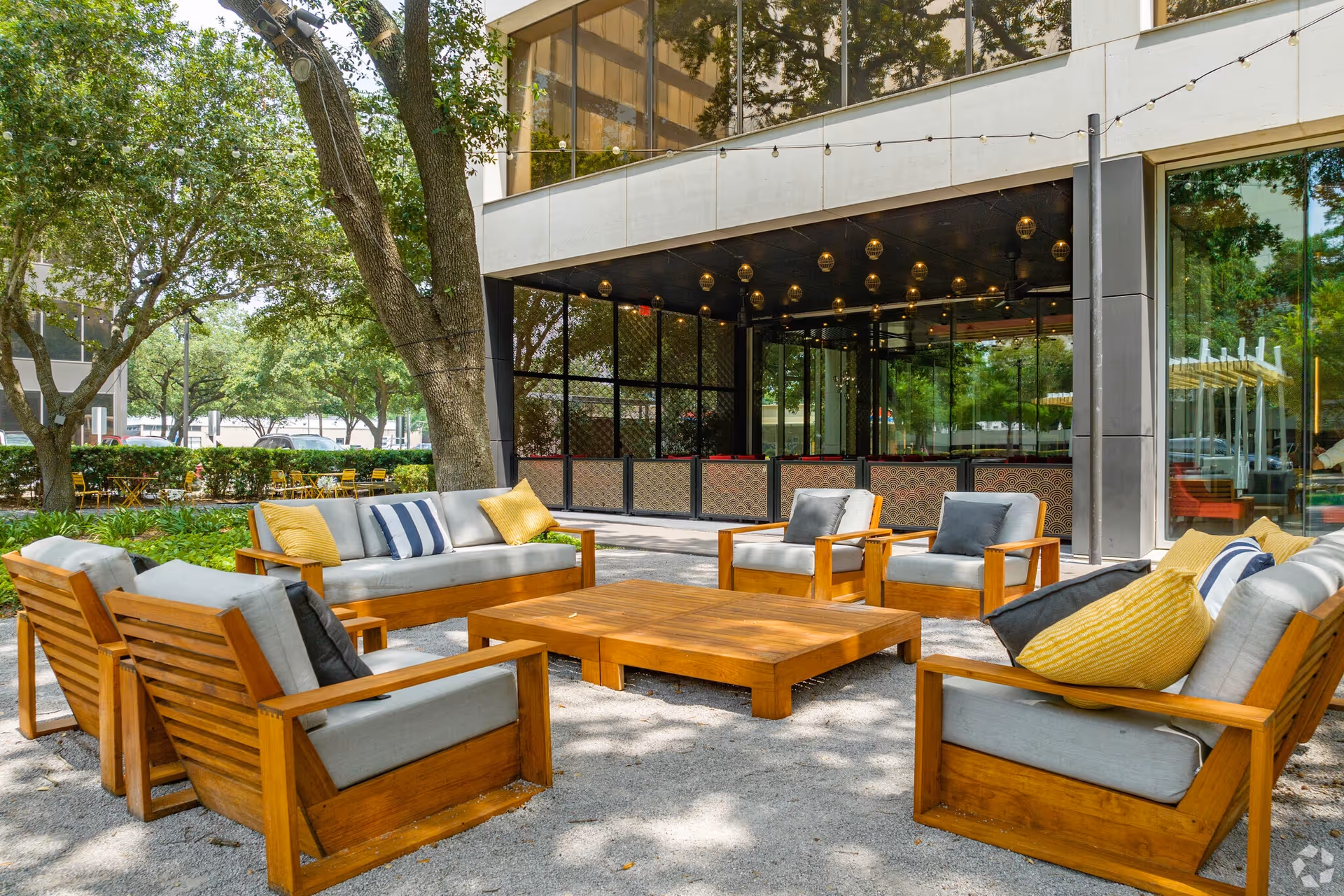 Outdoor lounge area with wooden seating and cushions beside a glass-front building