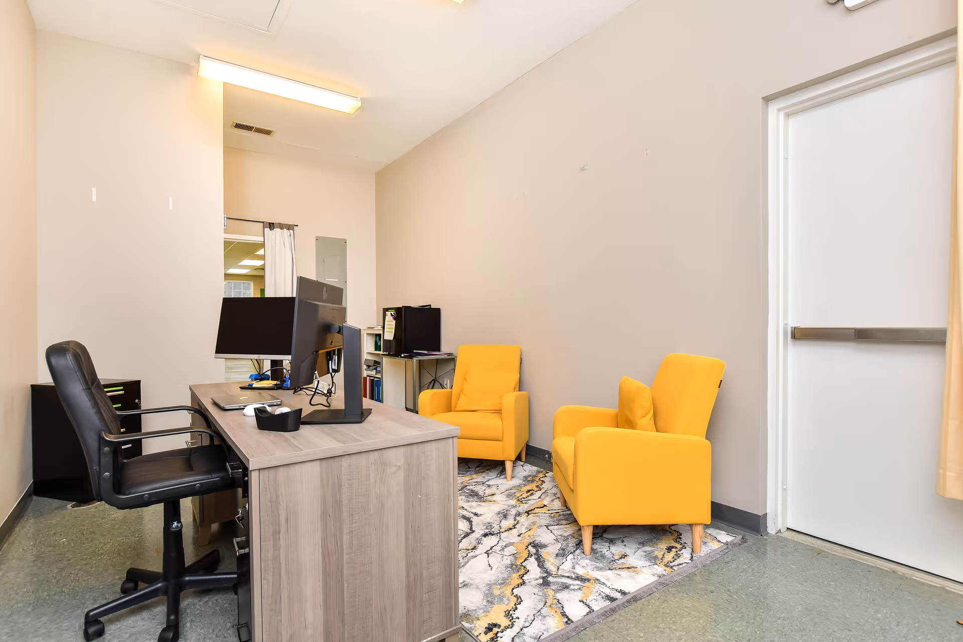 Office desk with computer and two yellow armchairs in a neutral lounge.