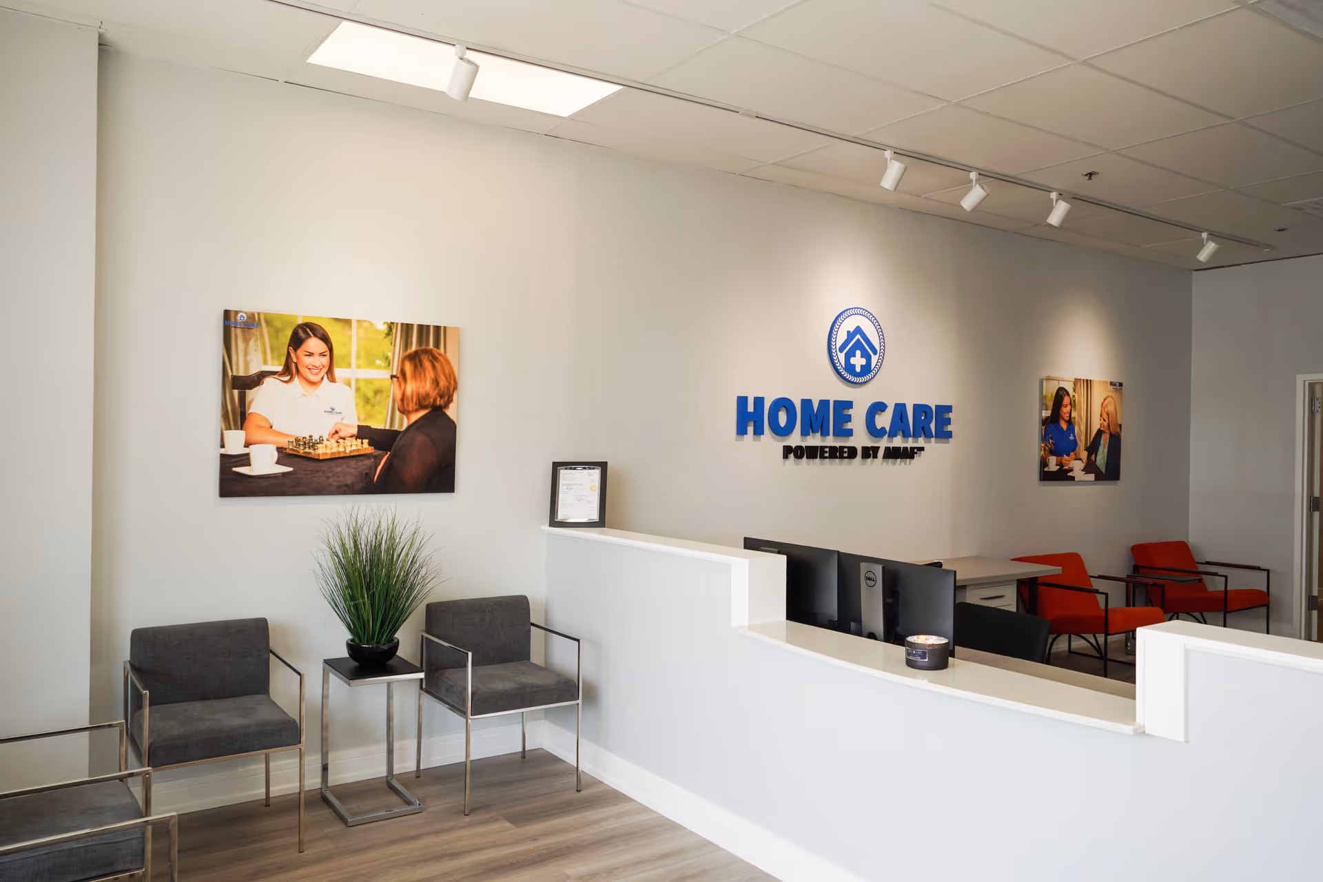 Reception area with curved counter, chairs, and a wall sign reading Home Care Powered by AUAF.