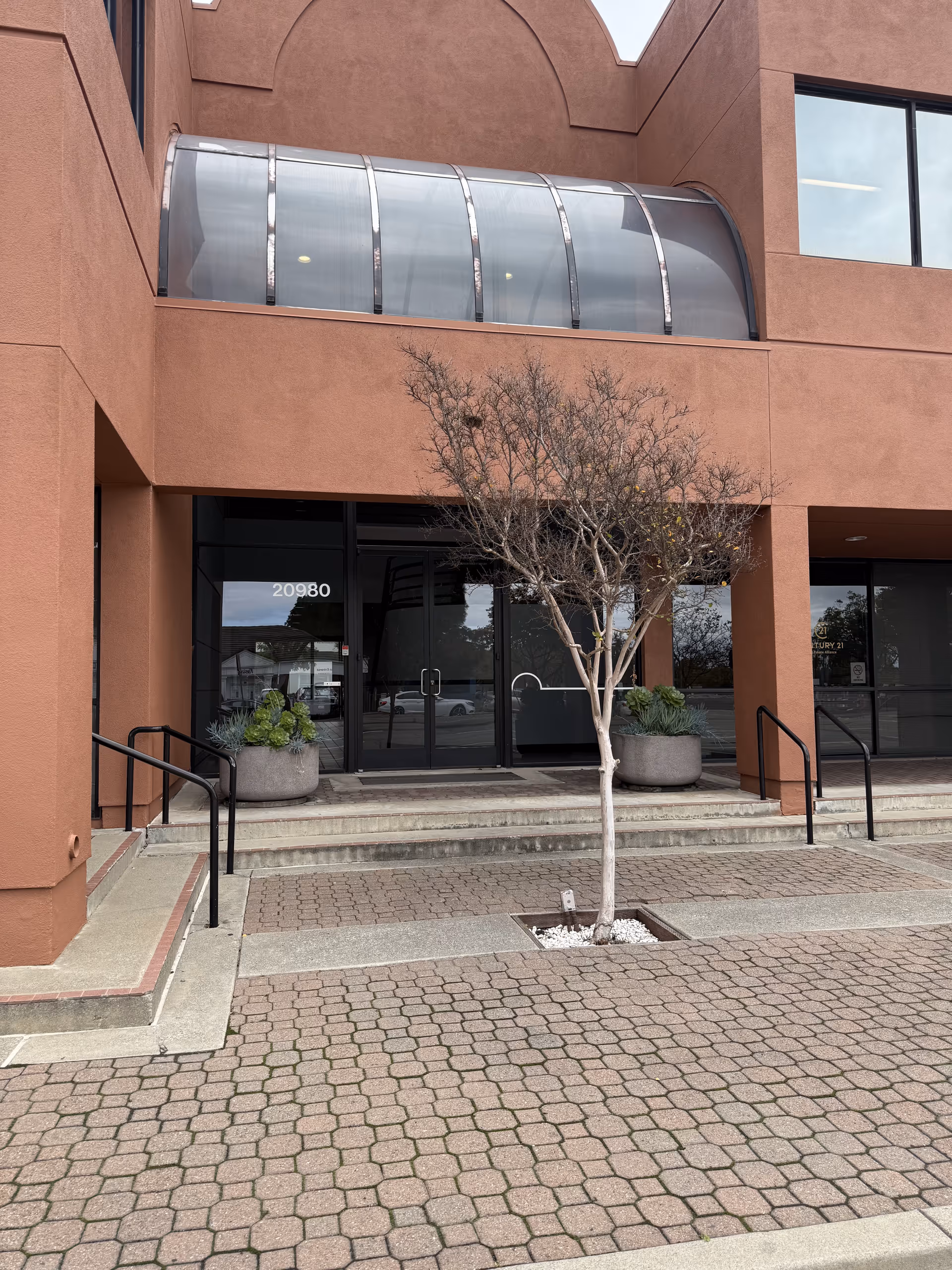 Exterior view of Right at Home facility entrance with glass canopy, steps, and tree.