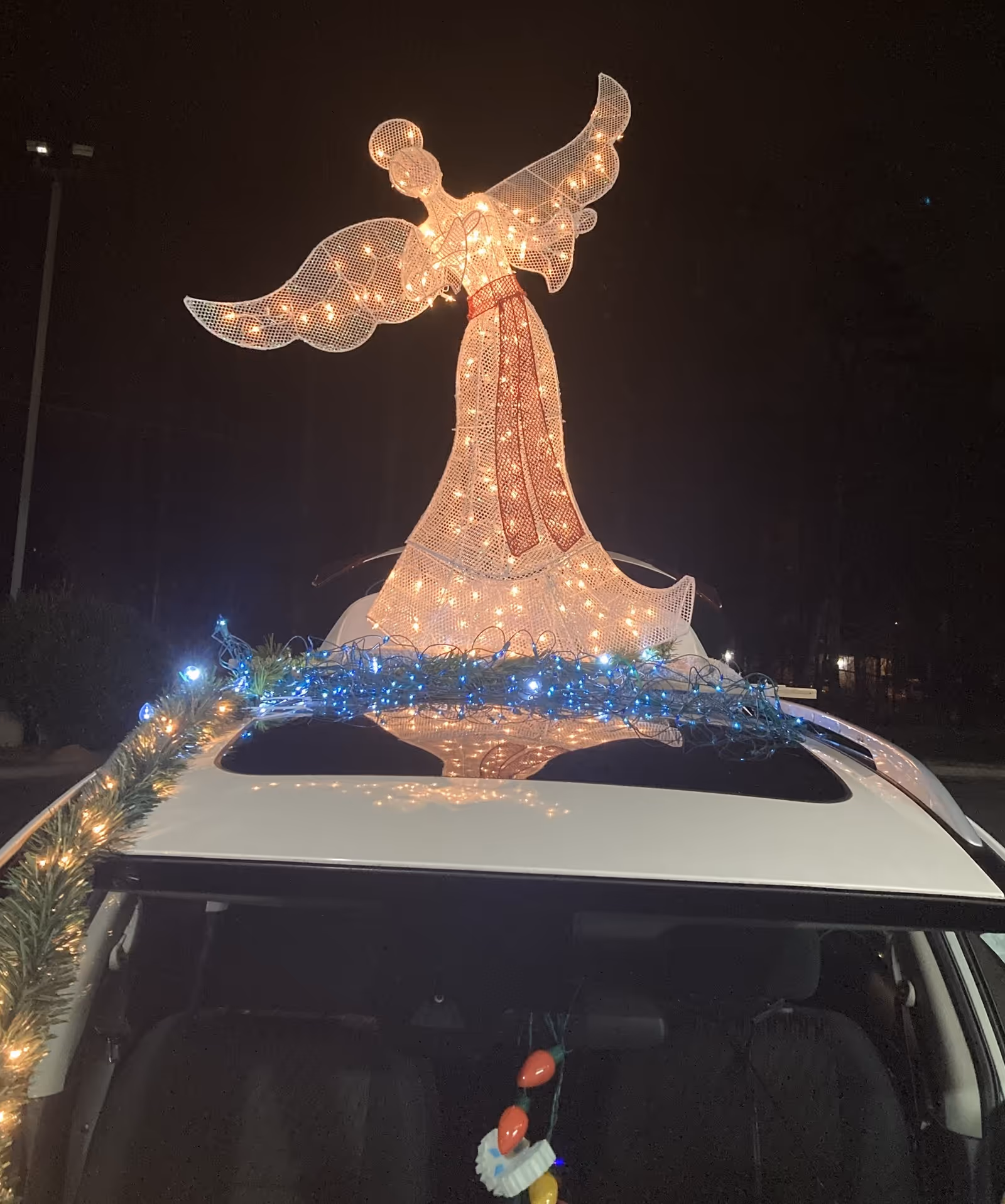 Night scene featuring a large illuminated angel decoration on a car roof.