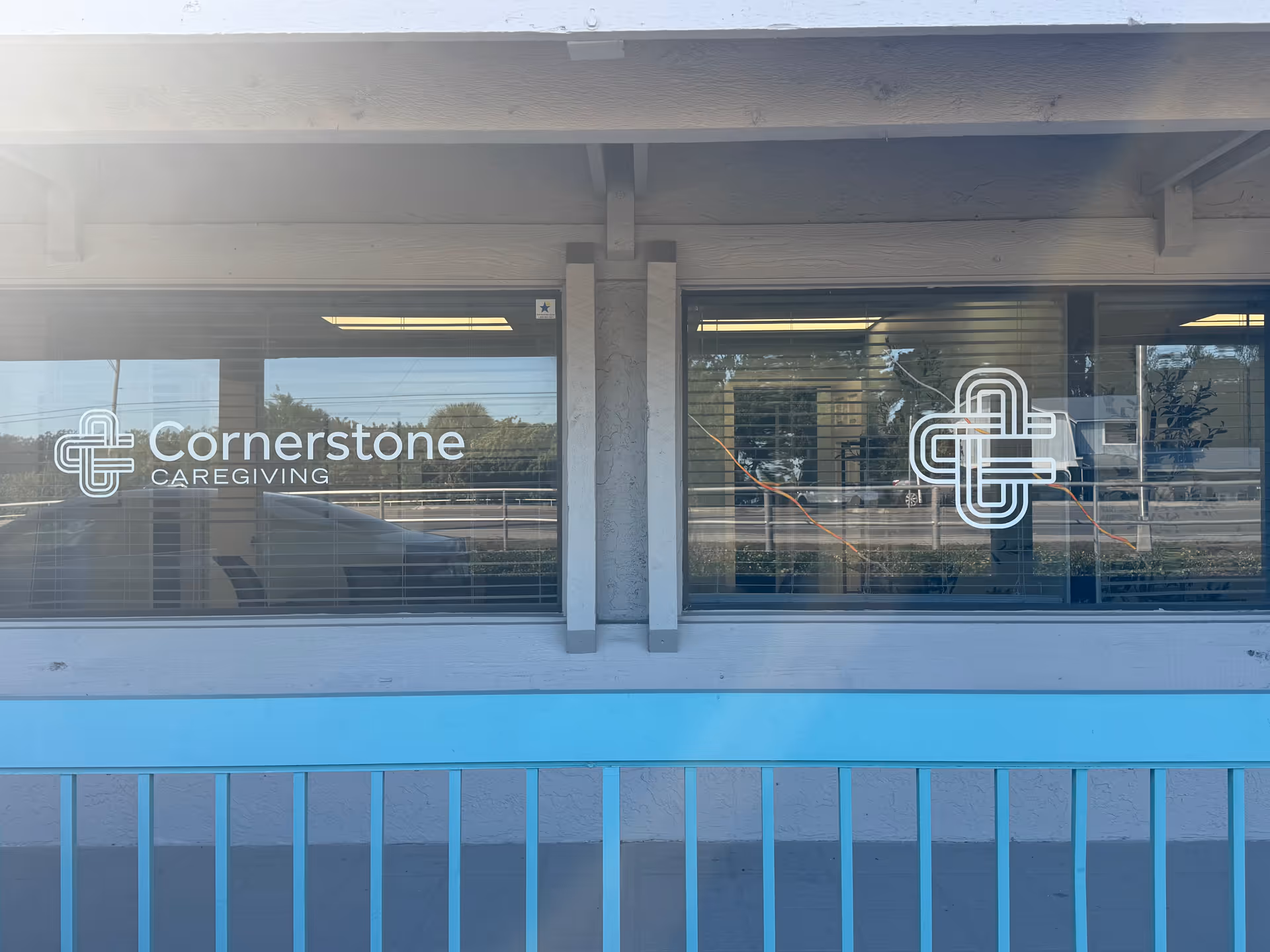 Facade of Cornerstone Caregiving building with glass windows displaying logos and a blue railing.