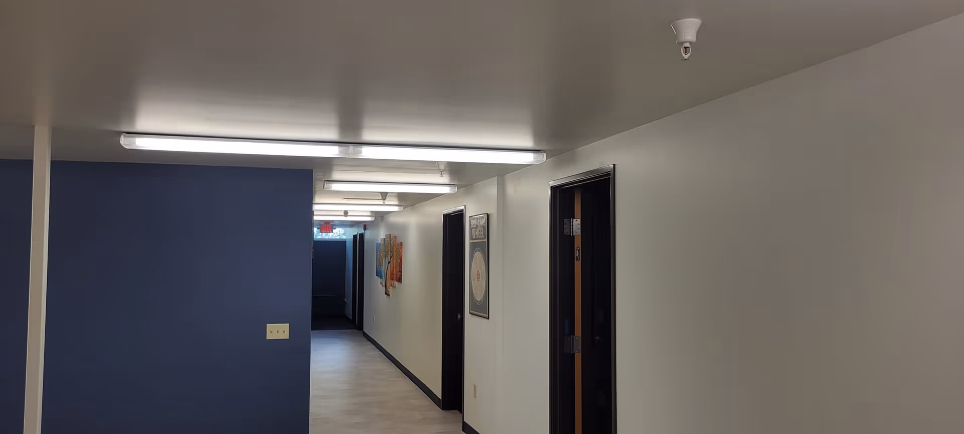 A long, well-lit interior corridor with doors on the right and a blue wall.