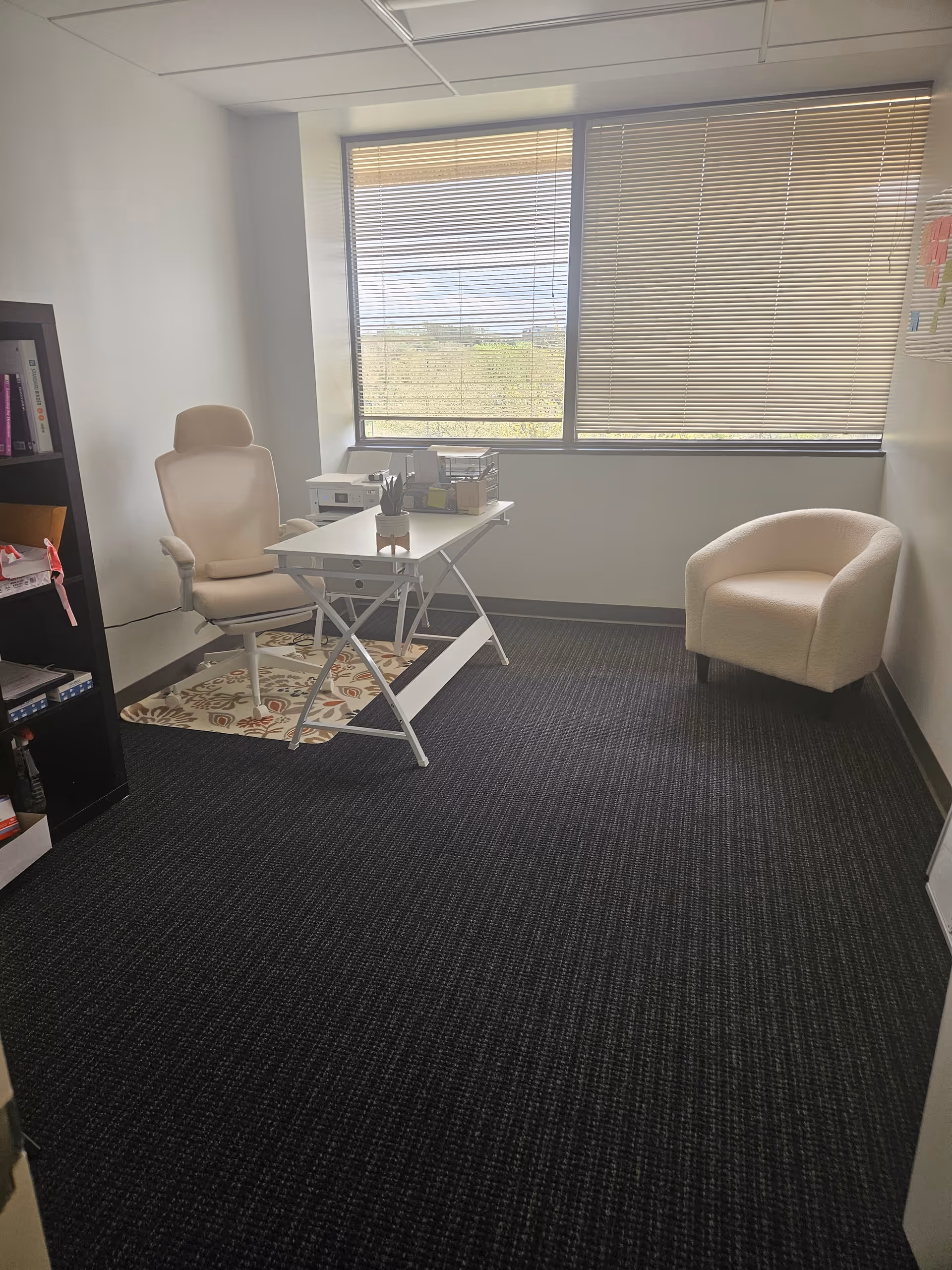 A small office with a desk, chair, shelves, and blinds in a senior living facility.