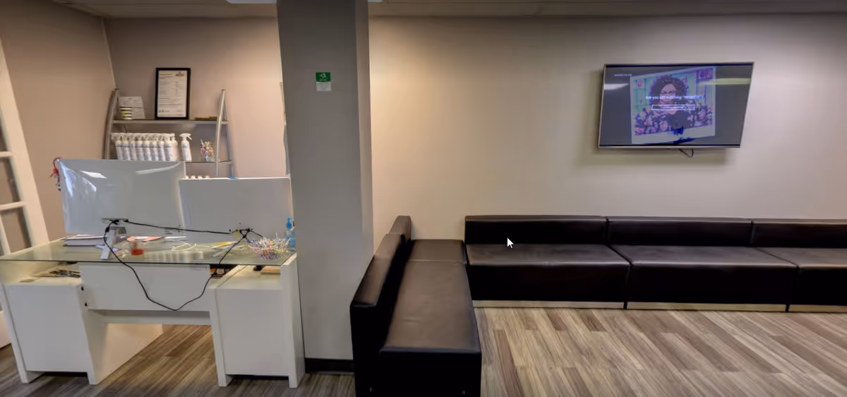 Interior lounge area with a glass-top desk, computer monitor, and black sectional seating.