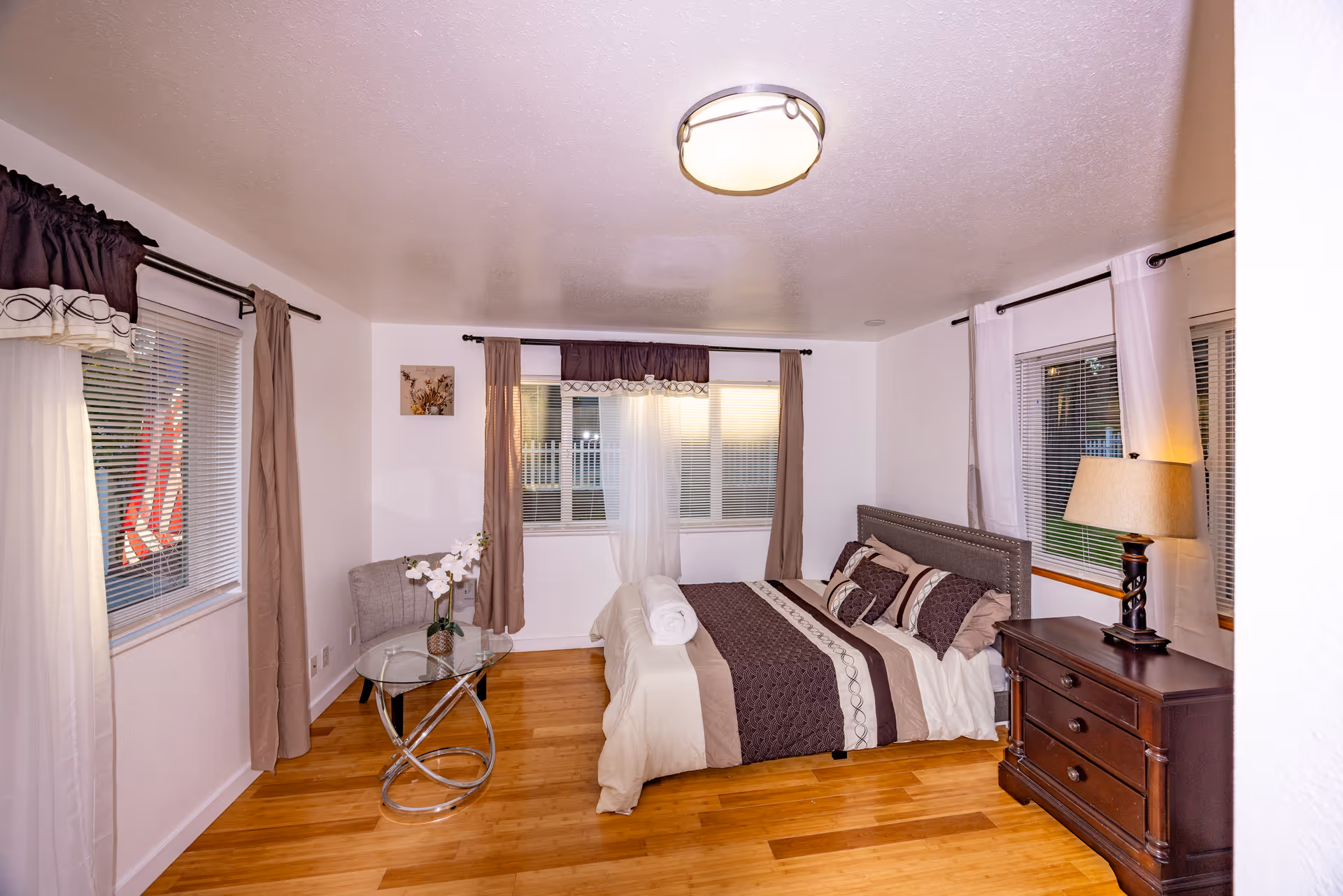 Bright bedroom with queen bed, nightstands, dresser, and windows with curtains.