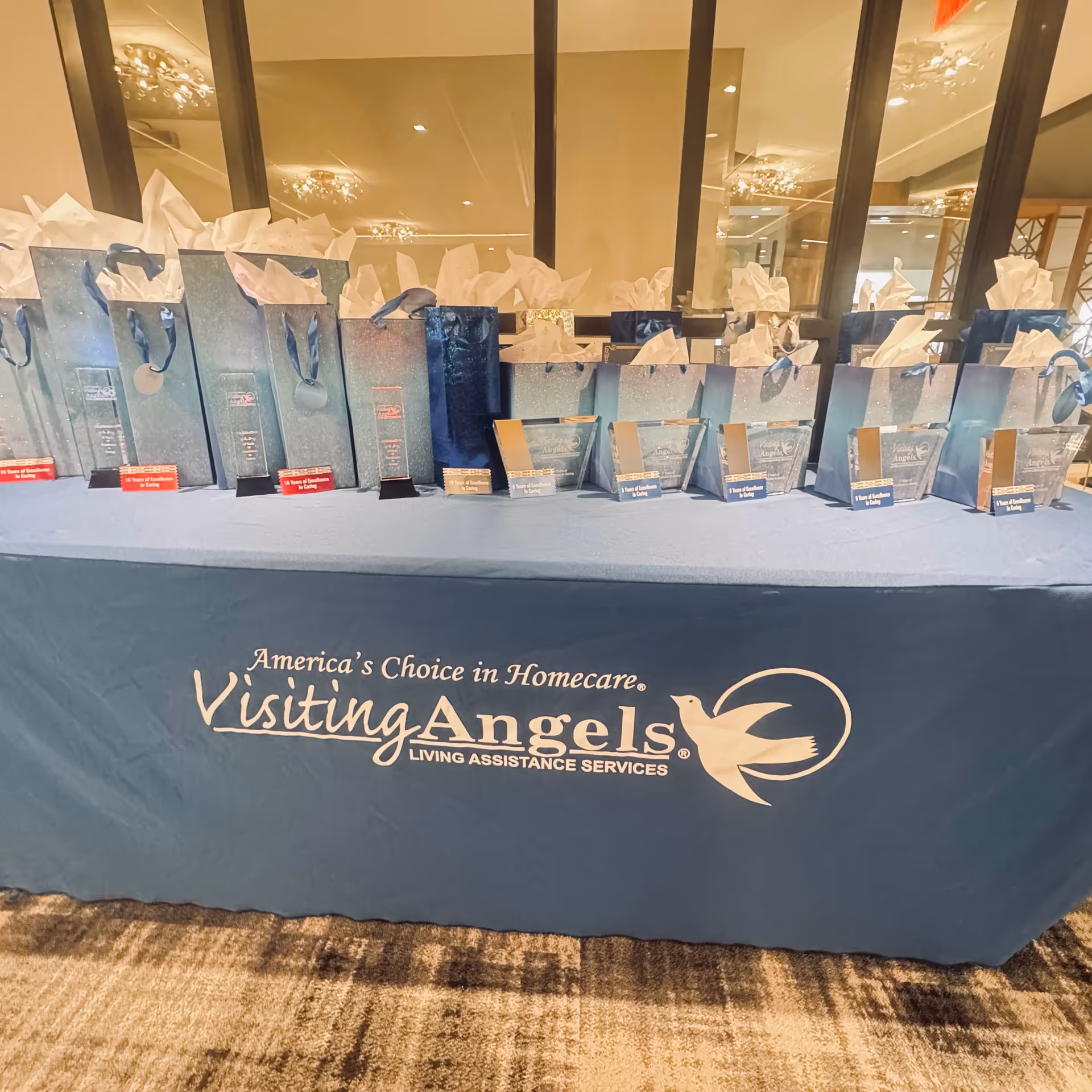 Table covered in blue cloth displays gift bags and boxes for Visiting Angels Senior Home Care.
