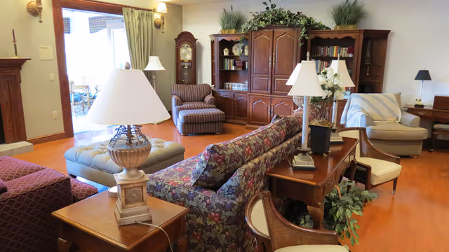 Cozy common living room with sofas, chairs, lamps, plants, and wooden cabinets.