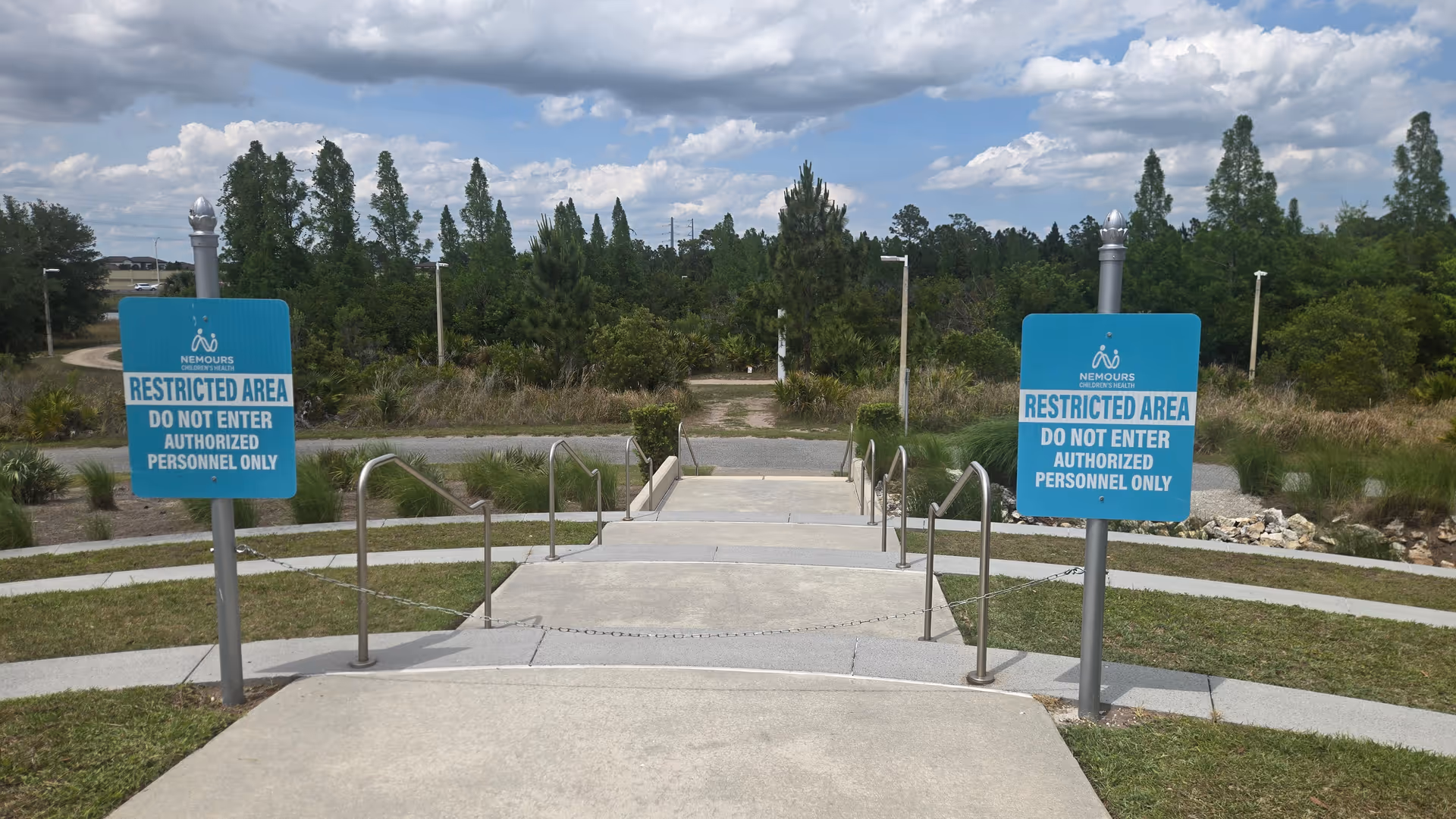 Outdoor pathway with stairs, stainless handrails, and blue Nemours restricted-area signs at a campus entrance.