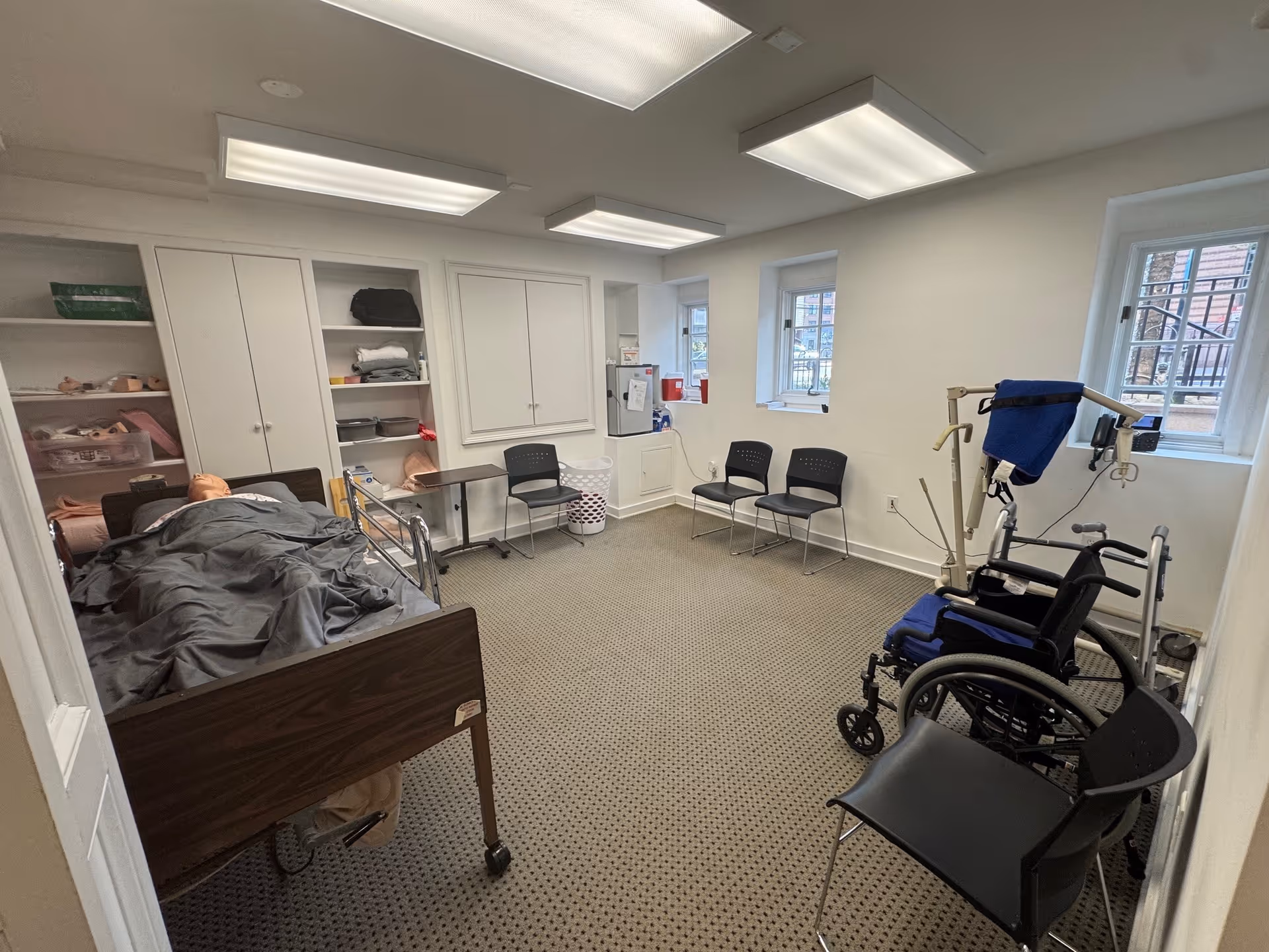 A BAYADA care room with a hospital bed, wheelchair, cabinets, and chairs.
