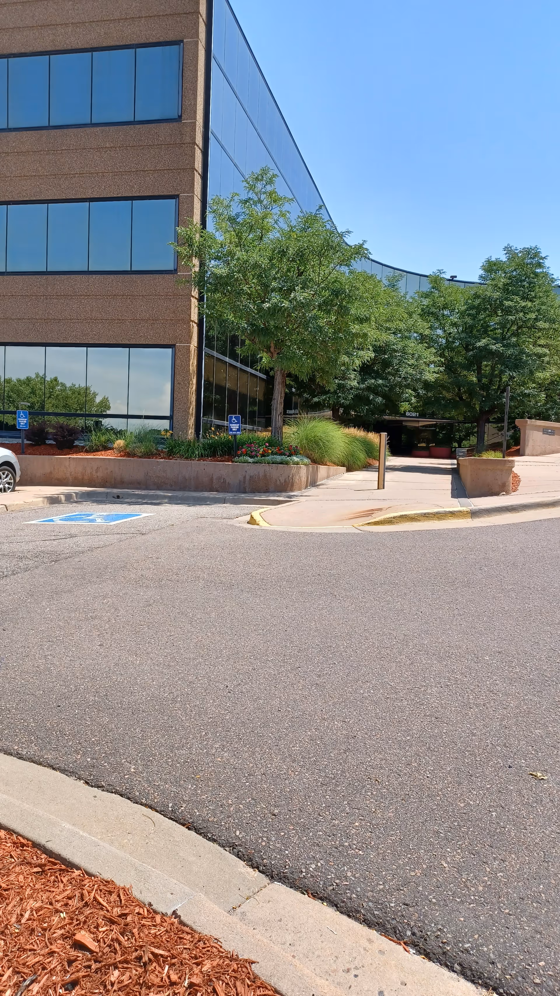 Exterior view of a modern brick-and-glass building with trees, landscaping, and a driveway entrance.