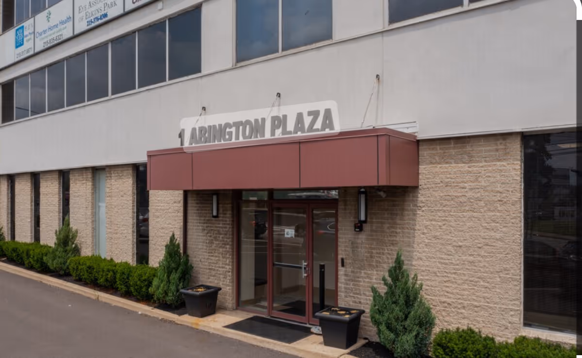 Exterior view of a building entrance with Abington Plaza sign and potted plants.