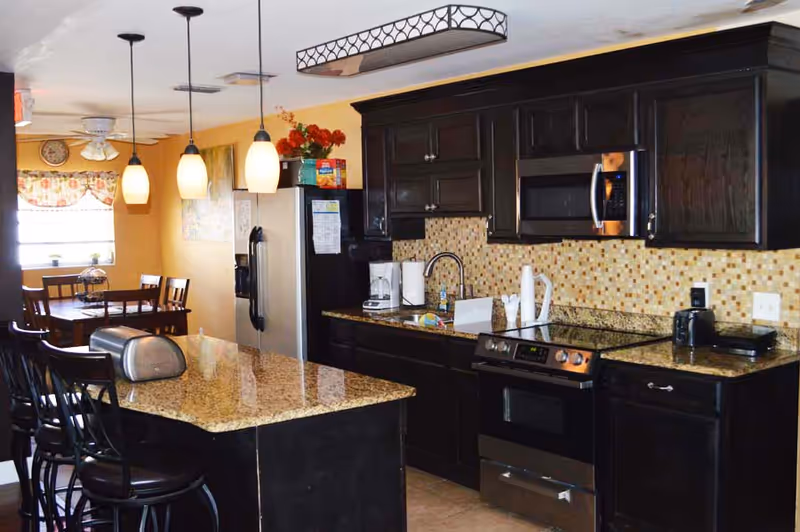 Dark wood kitchen with granite counters, island, stainless appliances, and a dining nook.