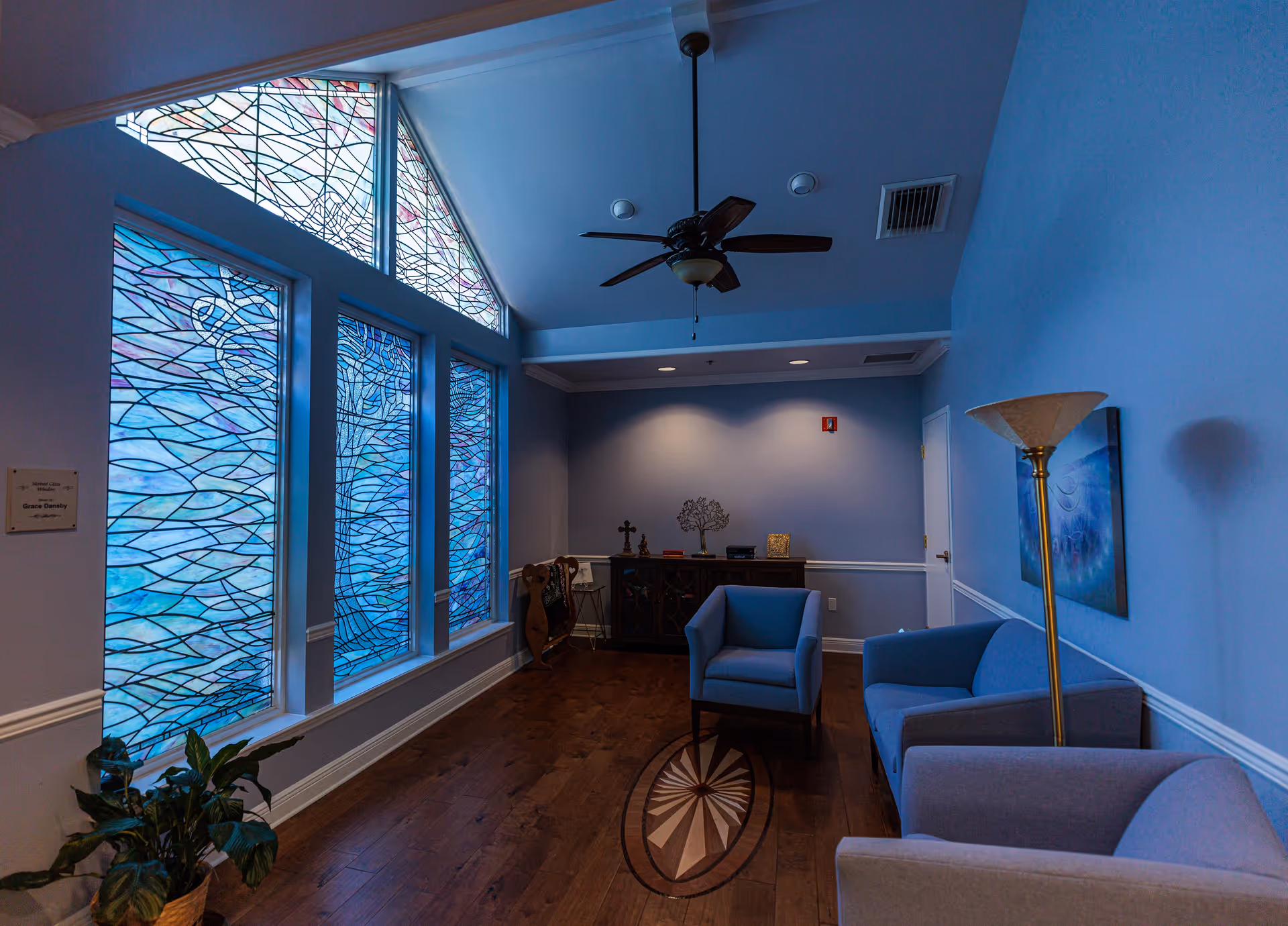 Blue-walled lounge with stained-glass windows, blue chairs, and a wooden floor.