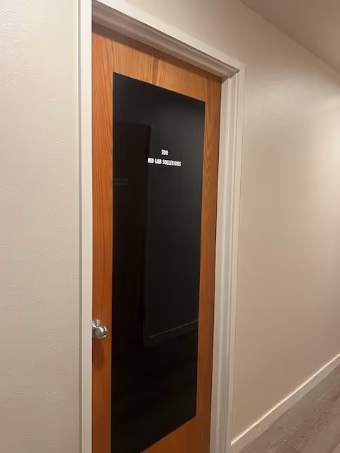 Interior hallway with a wooden door featuring a black glass panel labeled MD Lab Solutions.