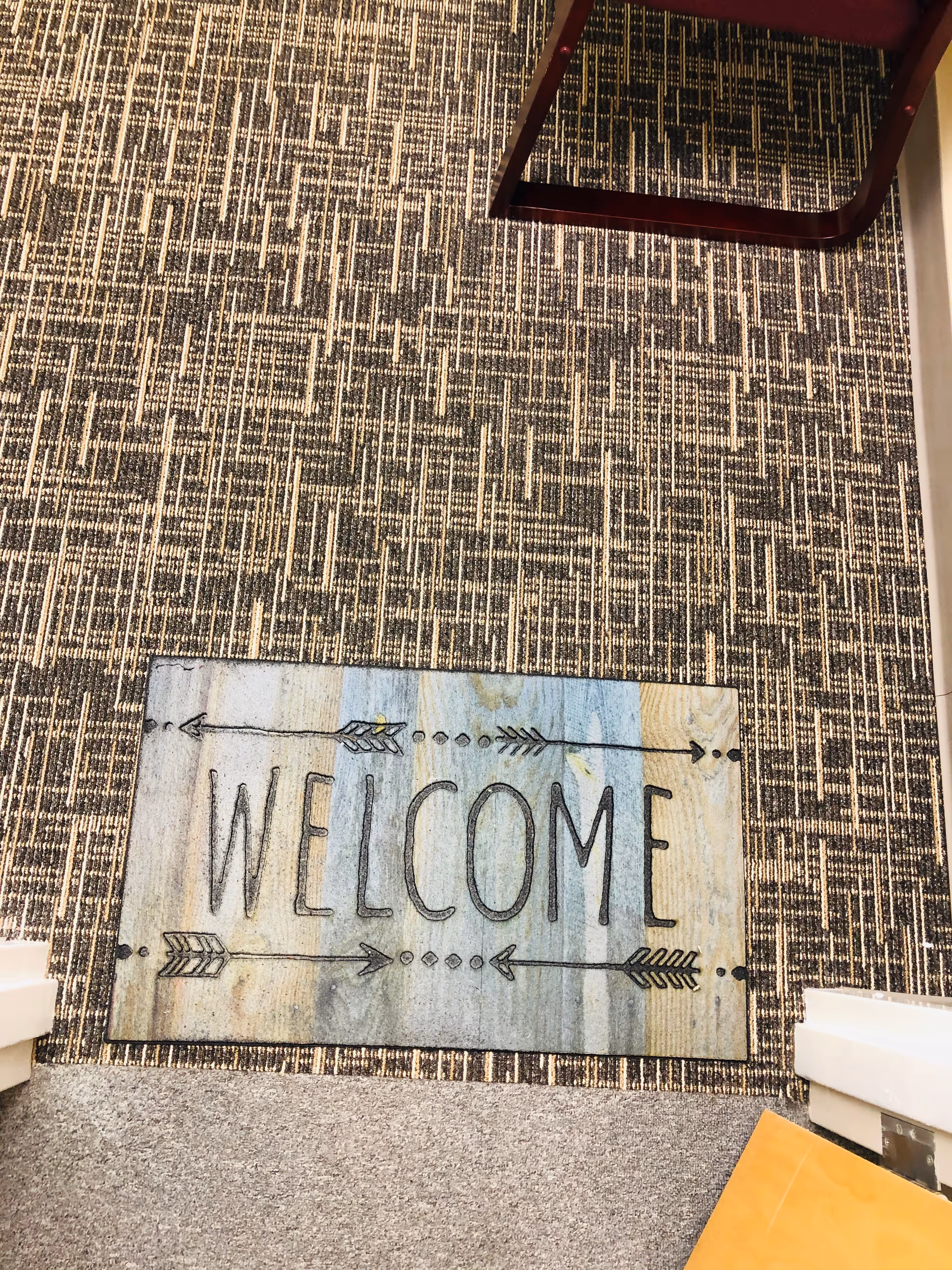 Interior facility entrance with decorative welcome mat on a patterned carpet.