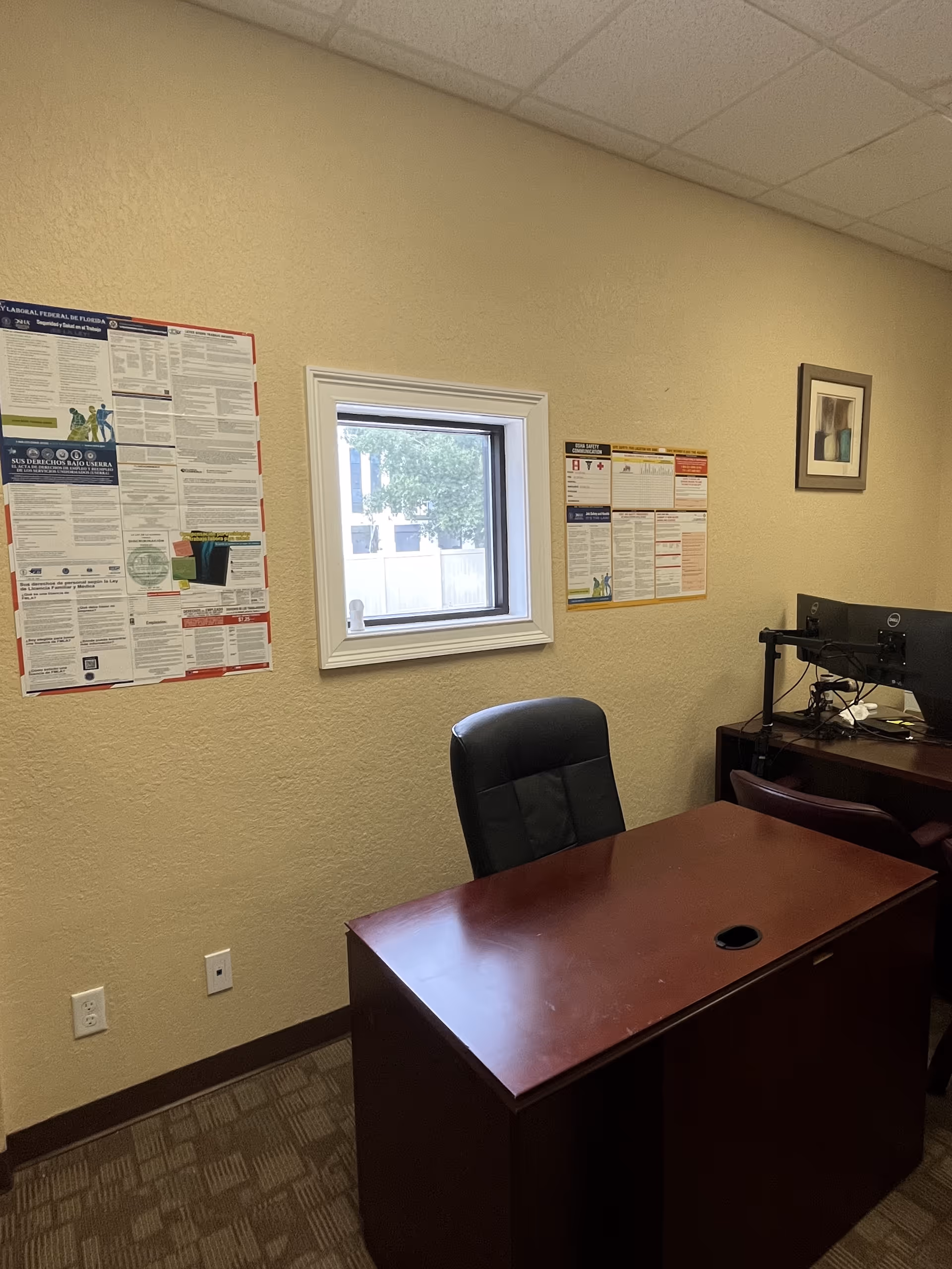 Office desk and chair in a small beige room with posters.
