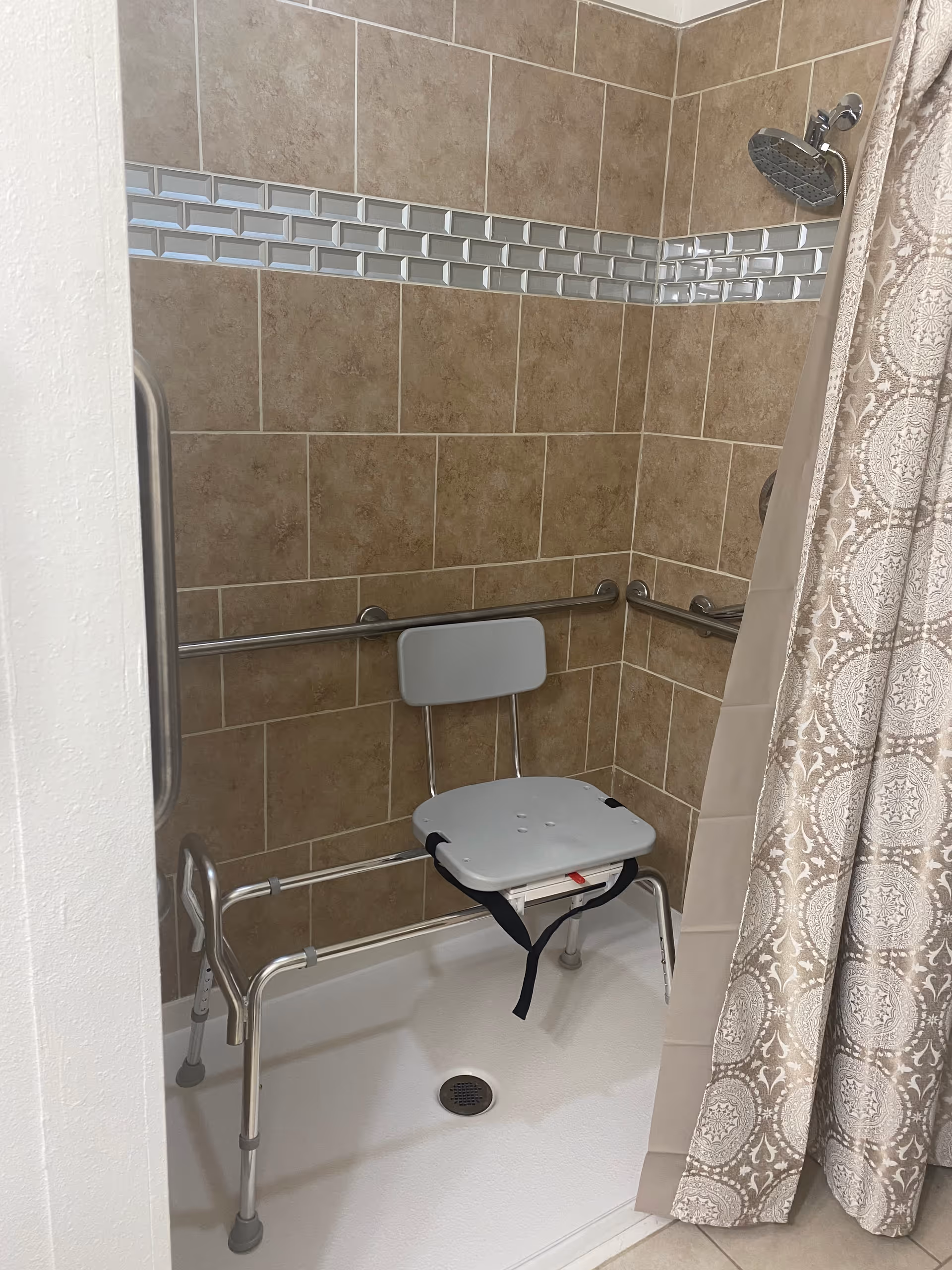 Accessible bathroom shower with a chair, grab bars, and tiled walls.