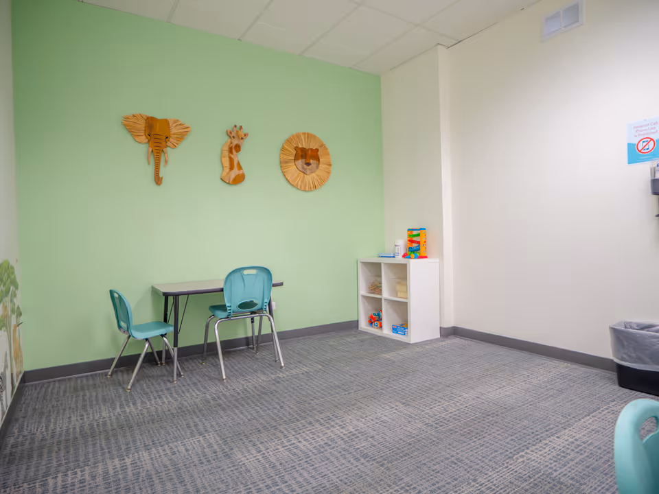 A small play area with a green wall, table, turquoise chairs, and a toy shelf.
