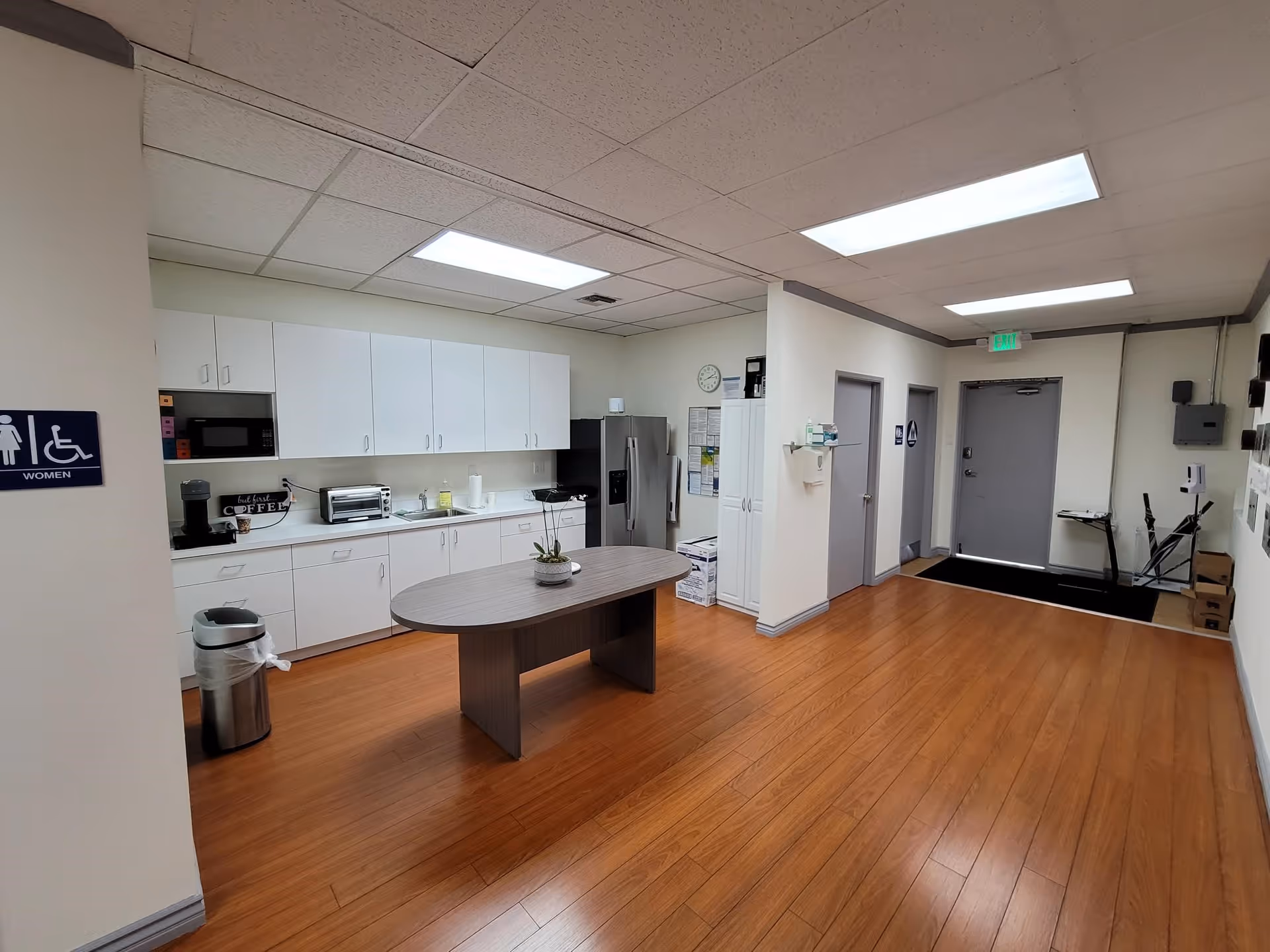 Bright communal kitchen with white cabinets, appliances, and a central oval table in a senior facility.