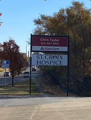 Roadside view of a St. Croix Hospice sign with trees and passing traffic.