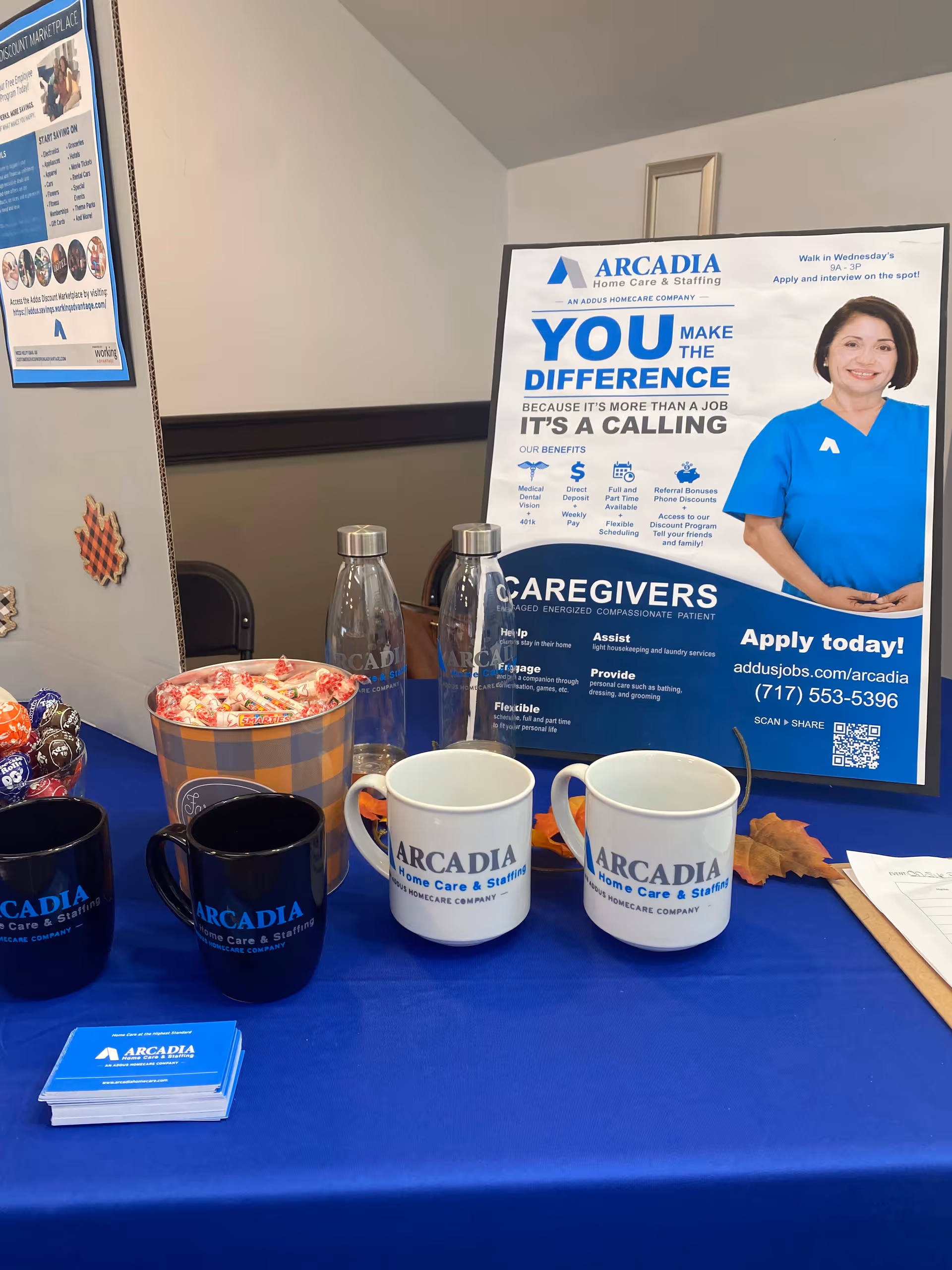 Indoor promotional booth featuring Arcadia signage, mugs, water bottles, and candy on a blue table.