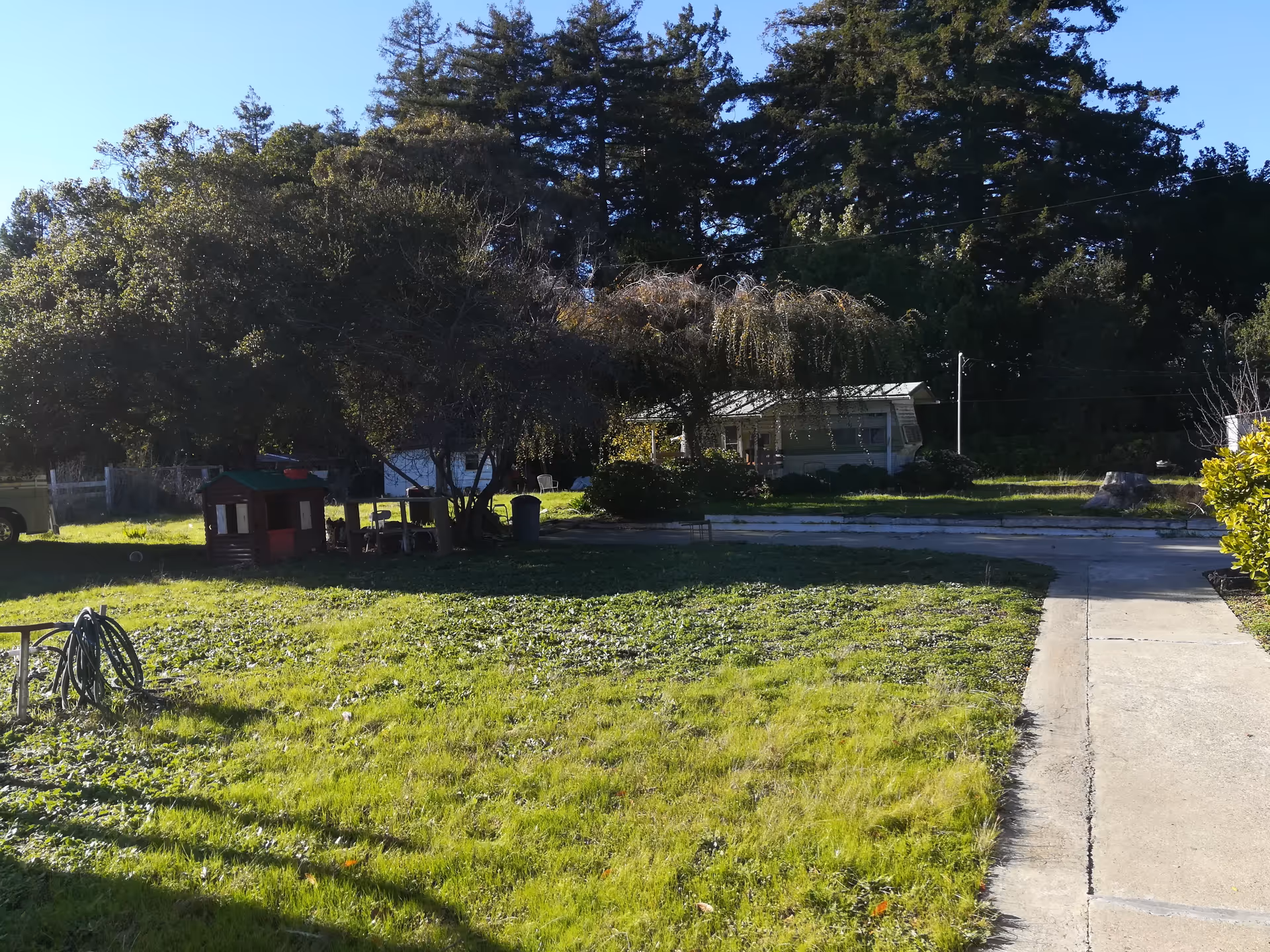 Outdoor front yard of a senior facility with trees, a small playhouse, and a distant building.