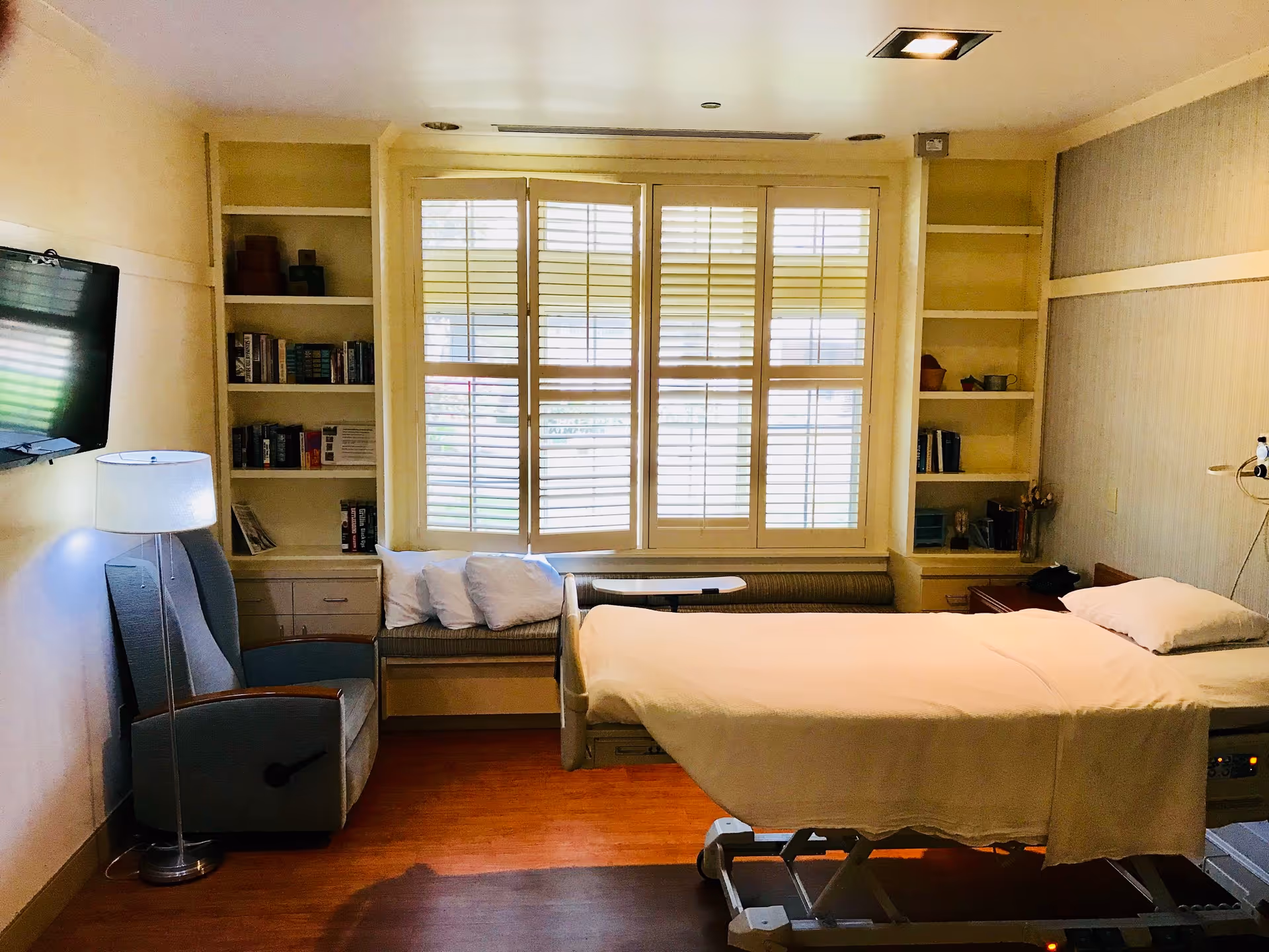 Senior living facility bedroom with a hospital-style bed, window, and built-in shelves.
