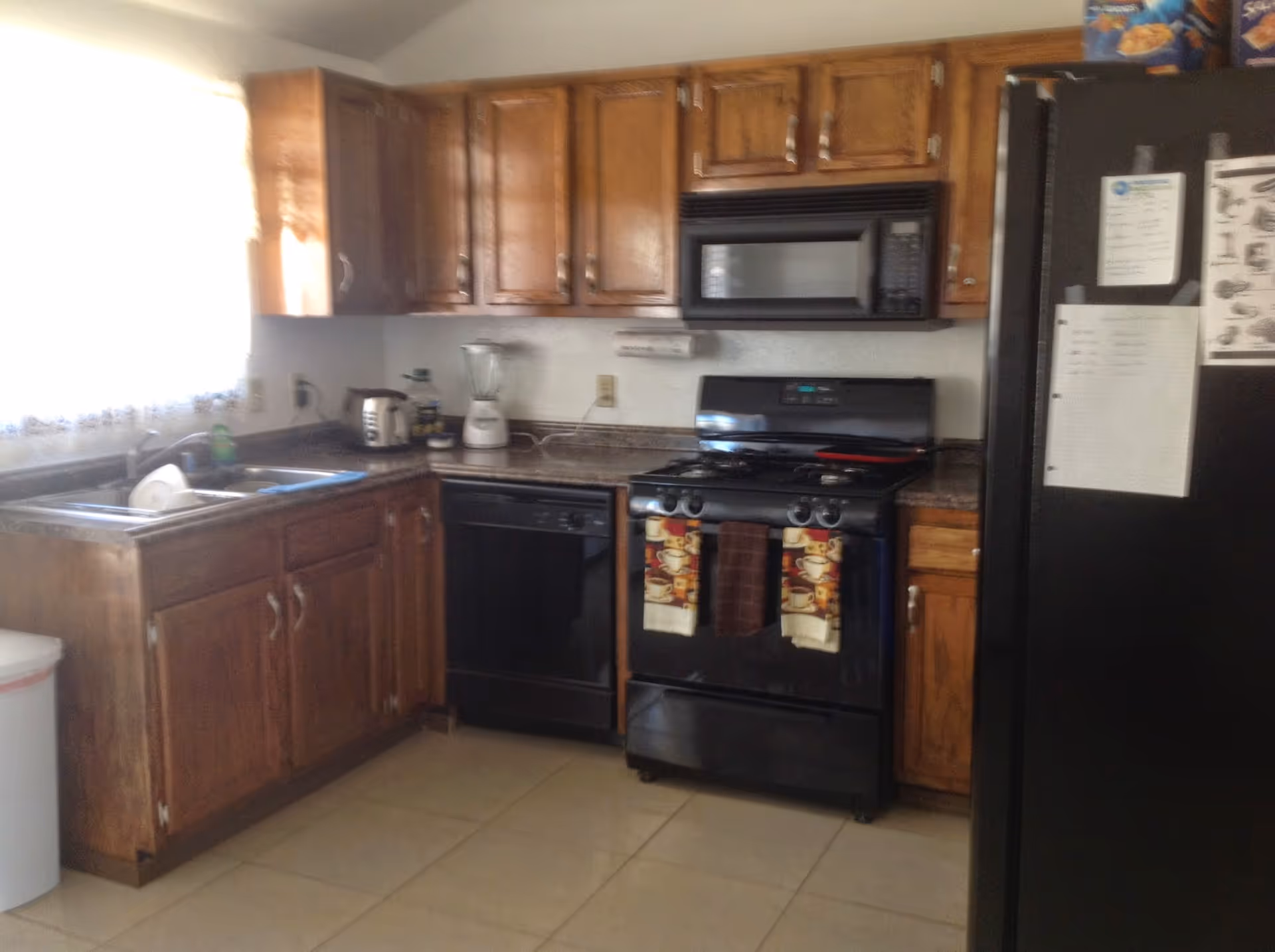 Compact kitchen with wooden cabinets, stove, microwave, sink, and black refrigerator.