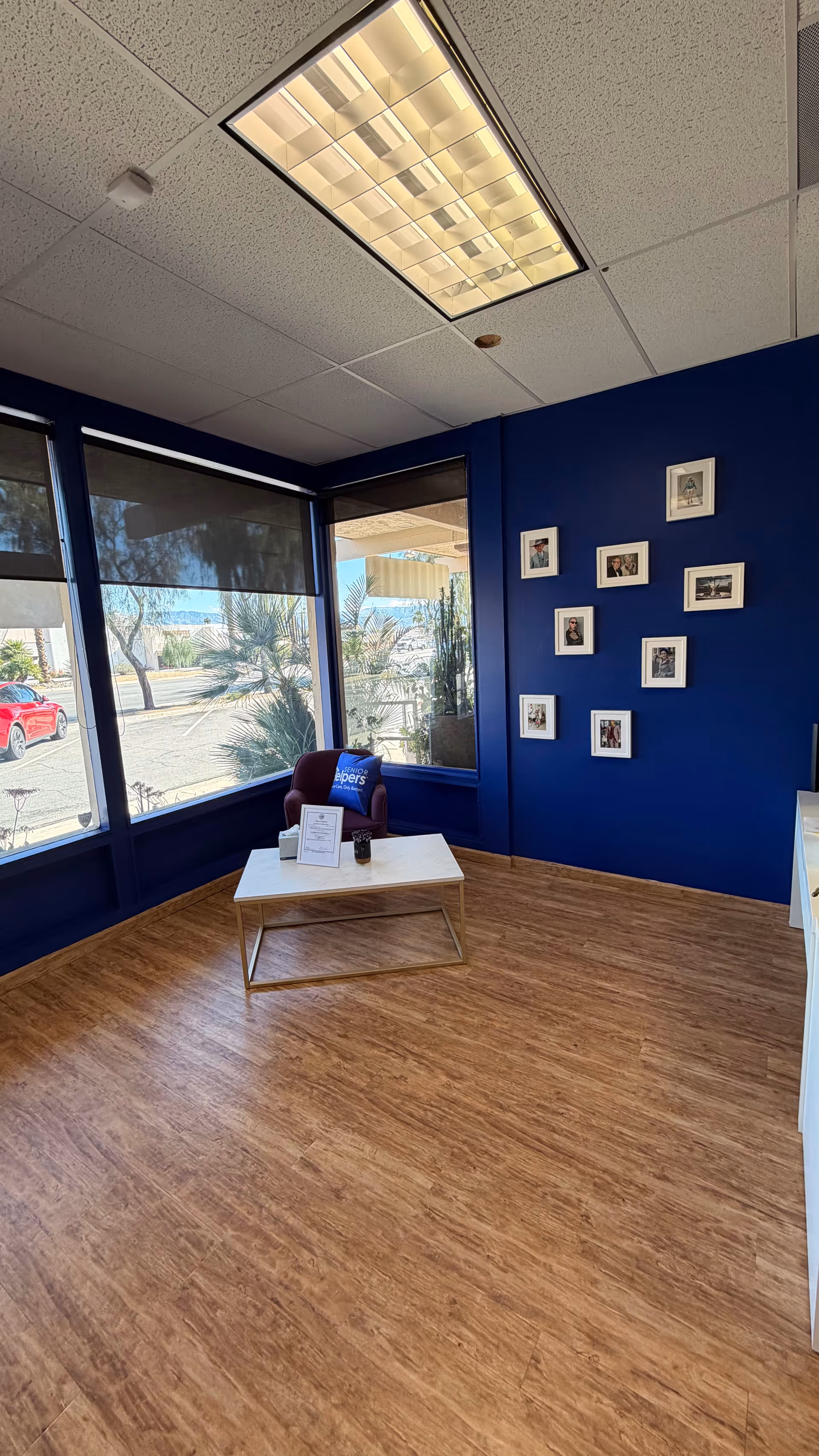 Small blue-walled lounge area with framed photos, large windows, and a white coffee table.