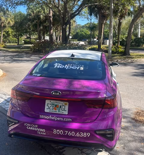 Purple Senior Helpers car parked in a sunny outdoor lot with trees.