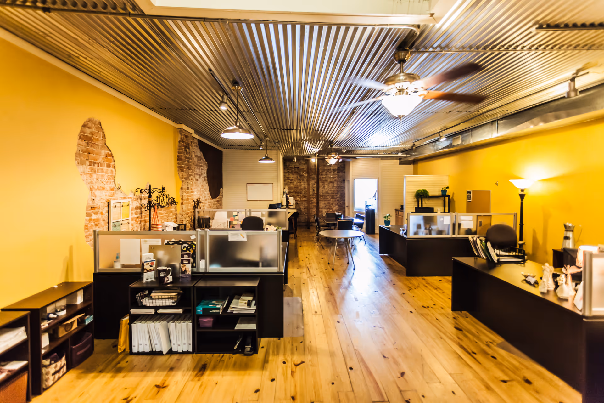 Bright yellow reception area with cubicles, desks, and wooden floors.