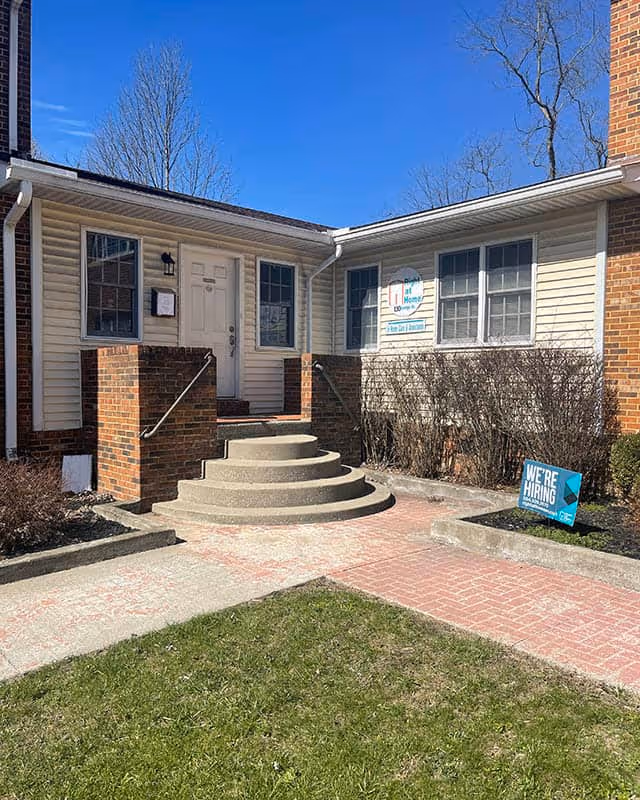 Front entrance of a senior living facility with steps, brick planters, and a We're Hiring sign.