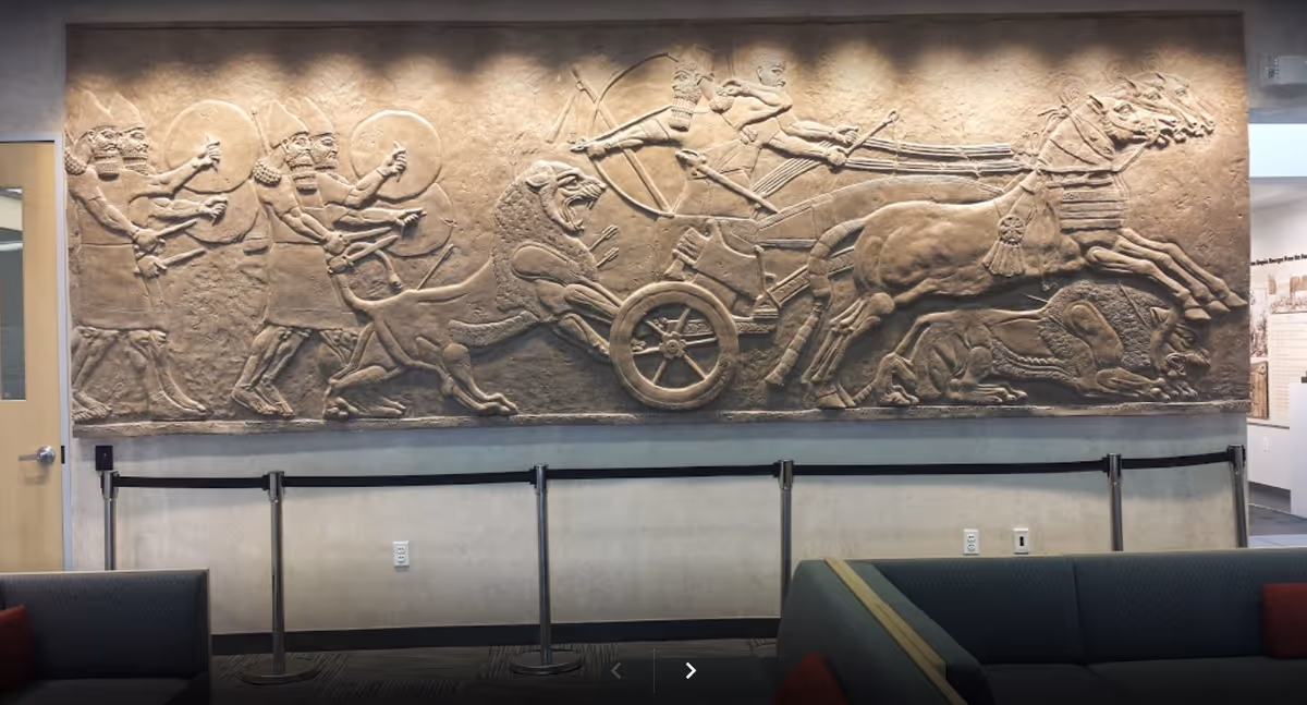 Indoor lobby features a large stone relief mural of chariots and figures.