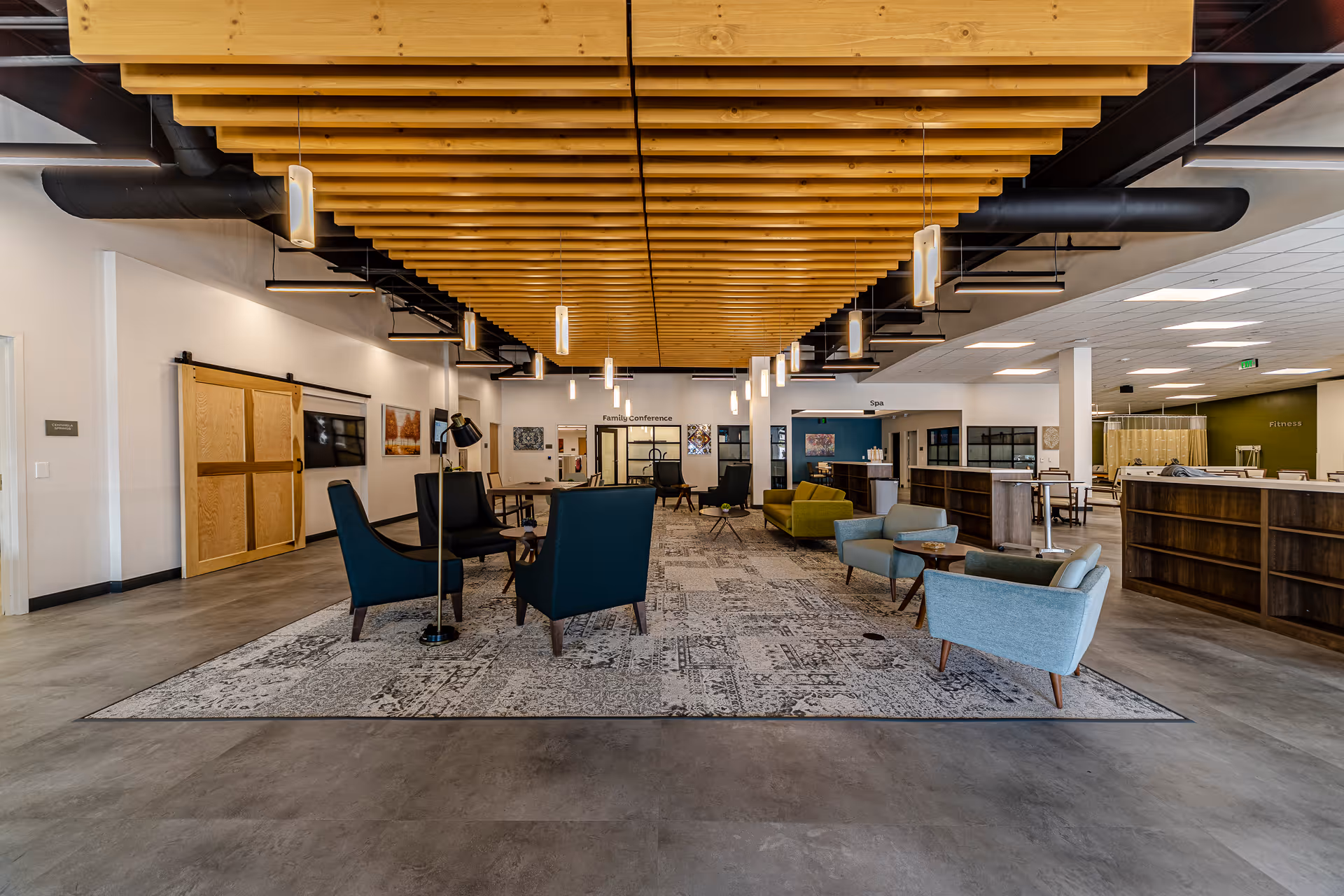 Open modern senior lounge with chairs, rugs, and wooden ceiling beams in spacious lobby.
